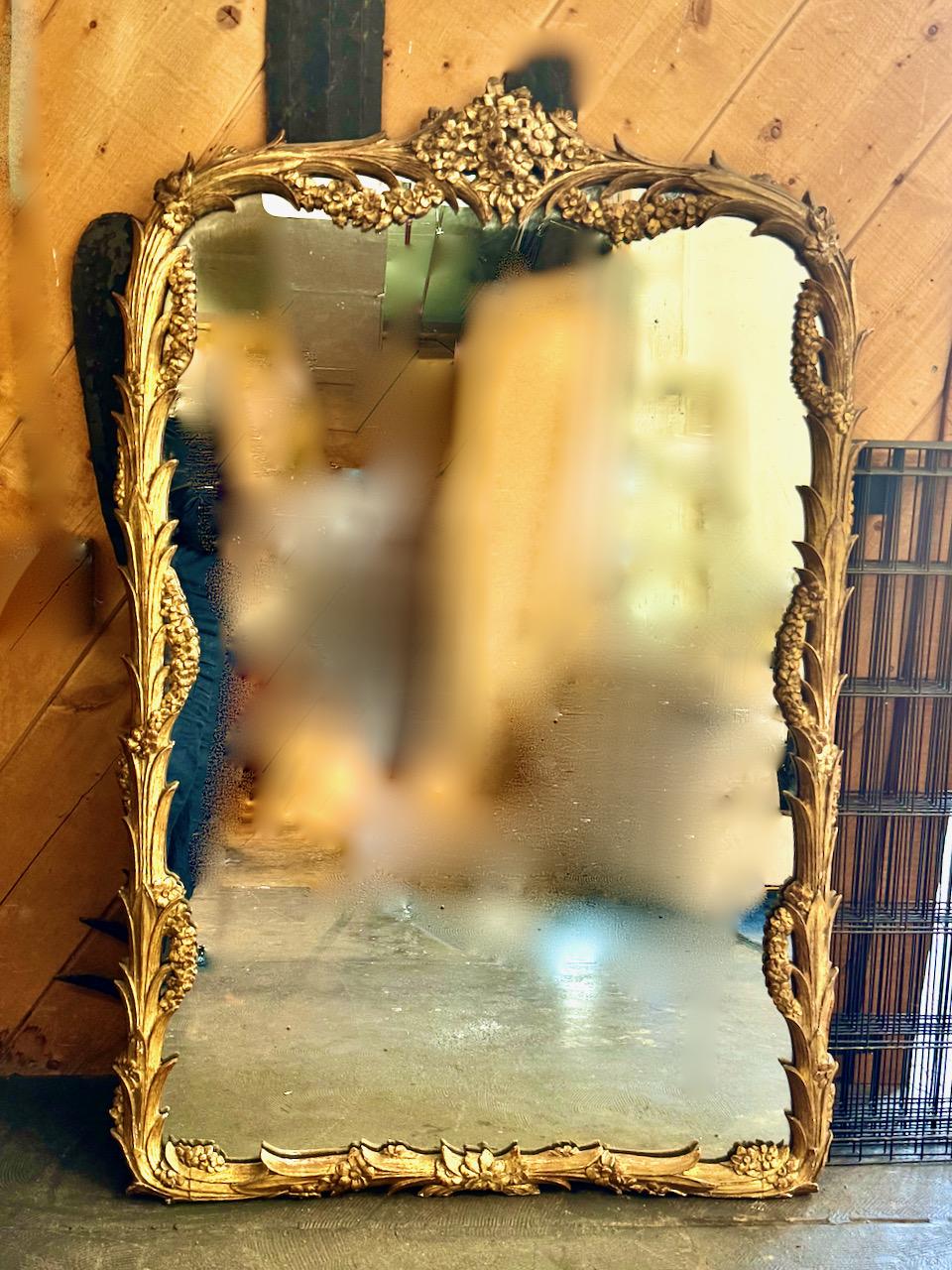 This is a very decorative Mantle or Full-Length mirror that dates to c. 1880-1910, the French Belle Epoque period. This mirror is beautifully carved with lily leaves and multiple flower swags. The mirror retains its original glass. and its original