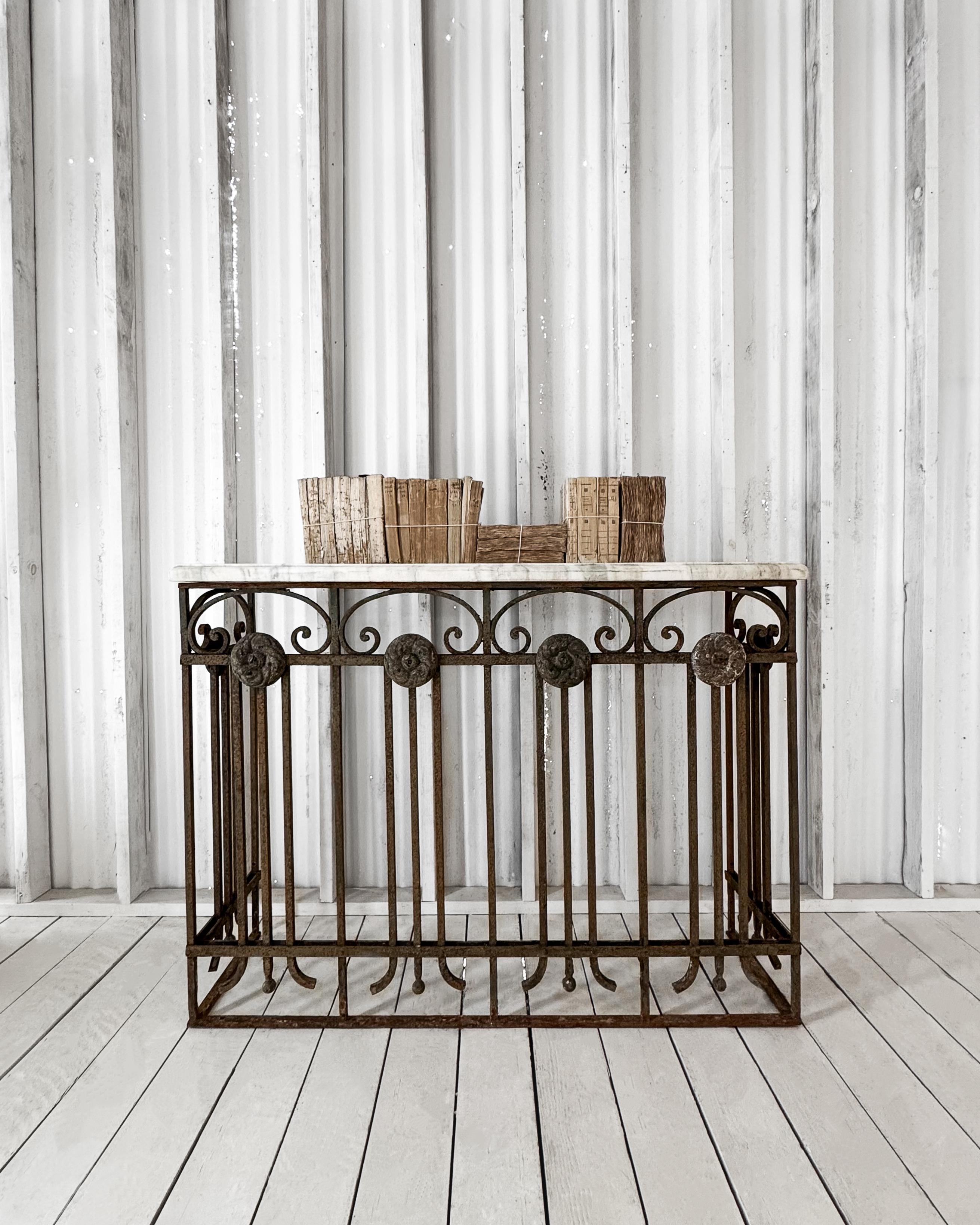 An antique Belle Époque console table featuring a sturdy (heavy!) cast iron base adorned with intricate scrollwork and decorative rosettes. A one-of-a-kind piece, the aged iron frame was once a gate panel, it retains a rich patina, lending a rustic