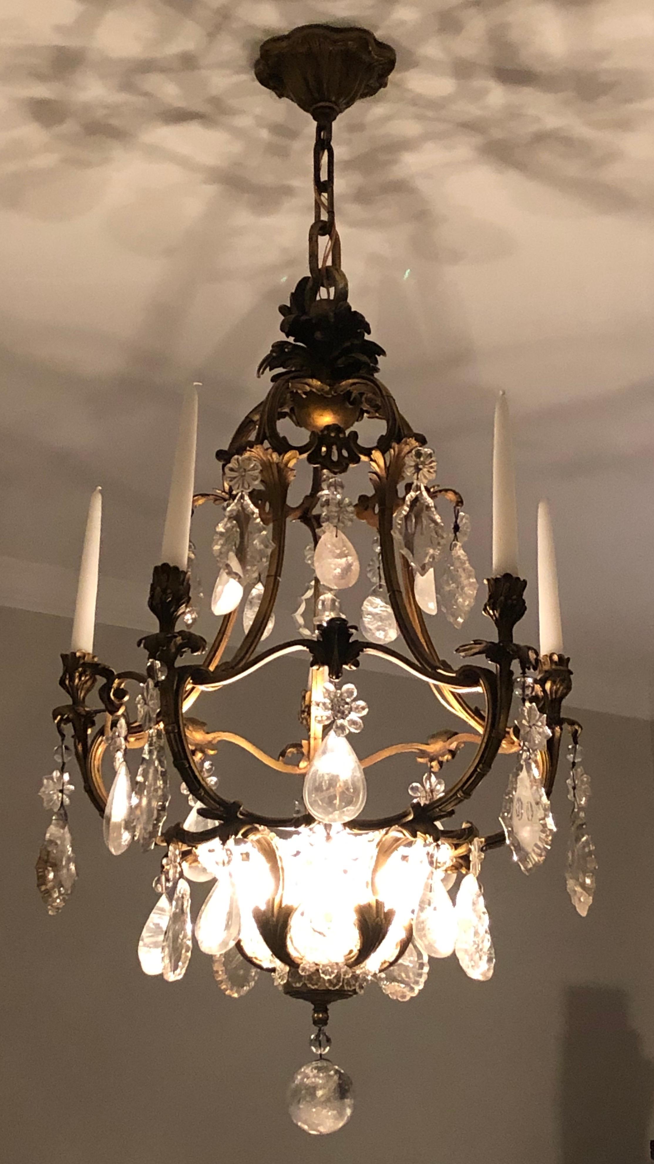 This chandelier was probably made by the Paris bronzier Baguès, circa 1900. The botanical forms of the cage, and the shapes of the rock-crystal prisms, recall the Rococo style of the 18th century.  But the sinuous cast-bronze curves channel the Art