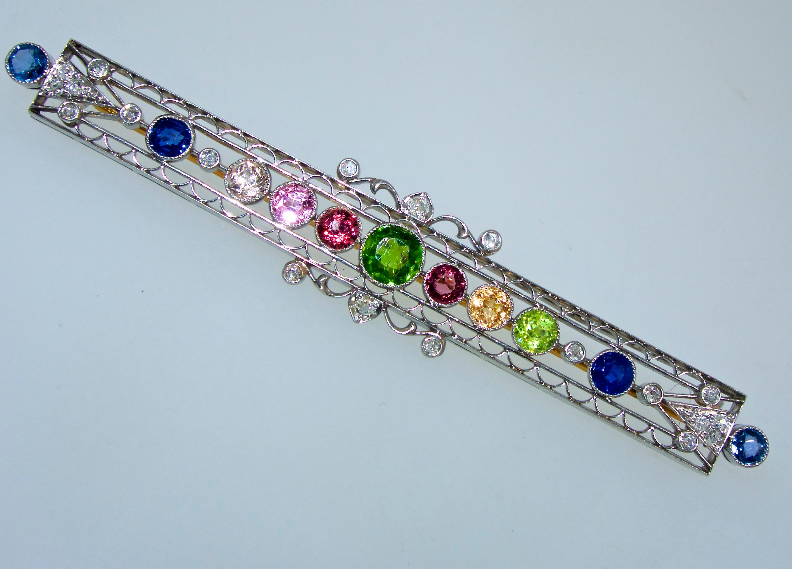 The center Demantoid green garnet is from the Ural Mountains in Russia and not mined today making this small 6.0 mm stone a rarity.  Flanked on both sides are fine bright sapphires, red garnets, topaz and diamonds.  This brooch is platinum topped