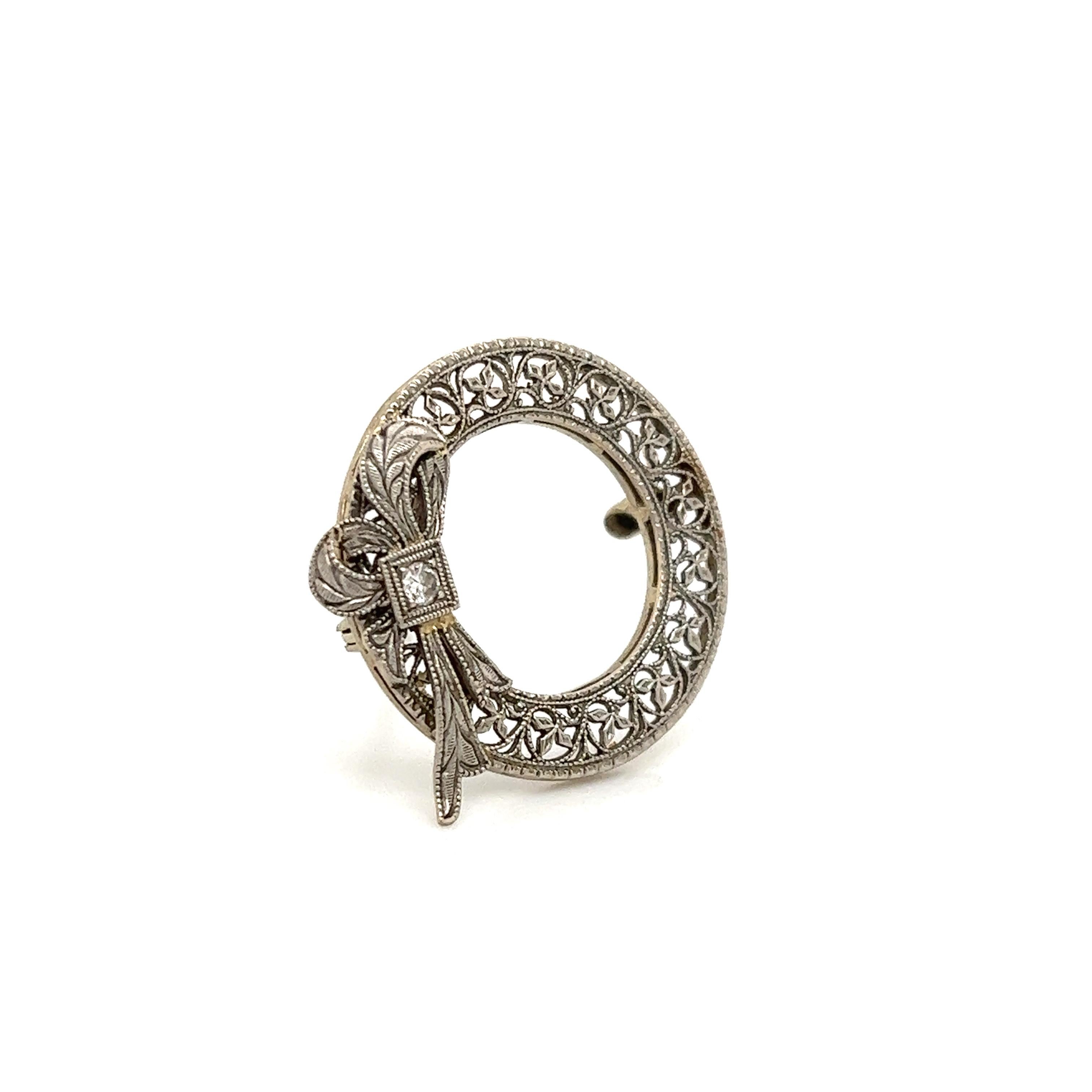 Elegant design seen on this brooch. The brooch is crafted in 14k white gold and is themed after the Belle Epoque era of jewelry. Whimsical filigree is crafted into the border of the brooch. The pin features an open work circular design and shows a