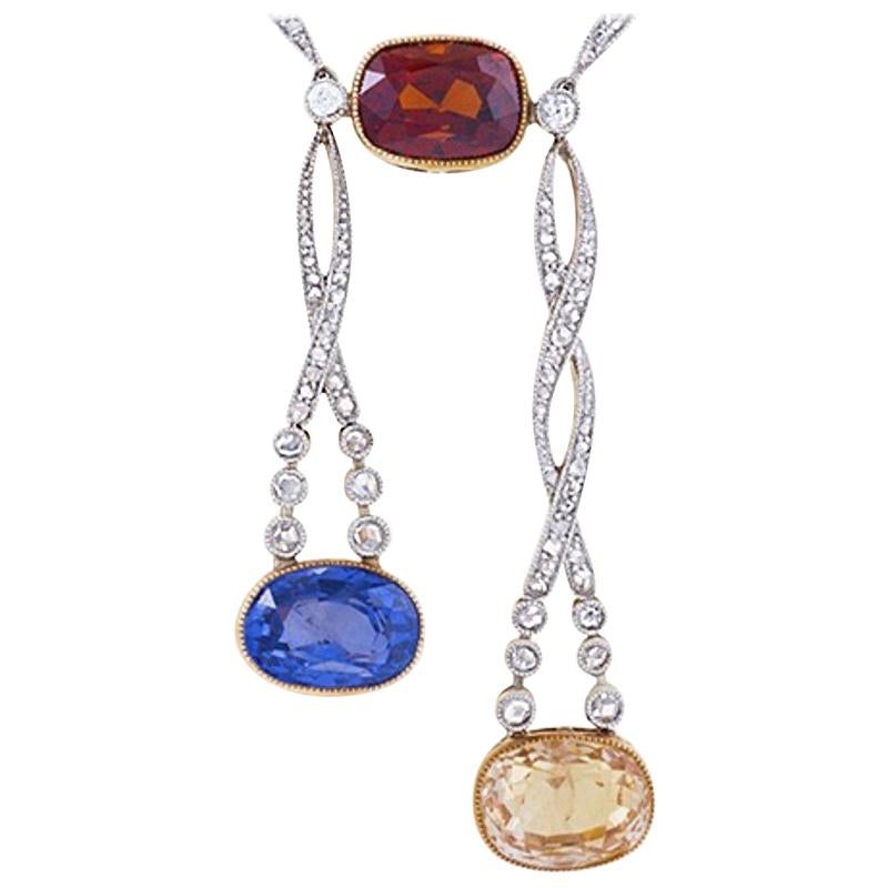 A Belle Epoque platinum and 14 karat gold lavaliere necklace with bezel-set garnet, yellow sapphire, blue sapphire and diamonds. The diamond-set platinum chain necklace suspends a cushion-shape red garnet with an approximate weight of 5.50 carats,