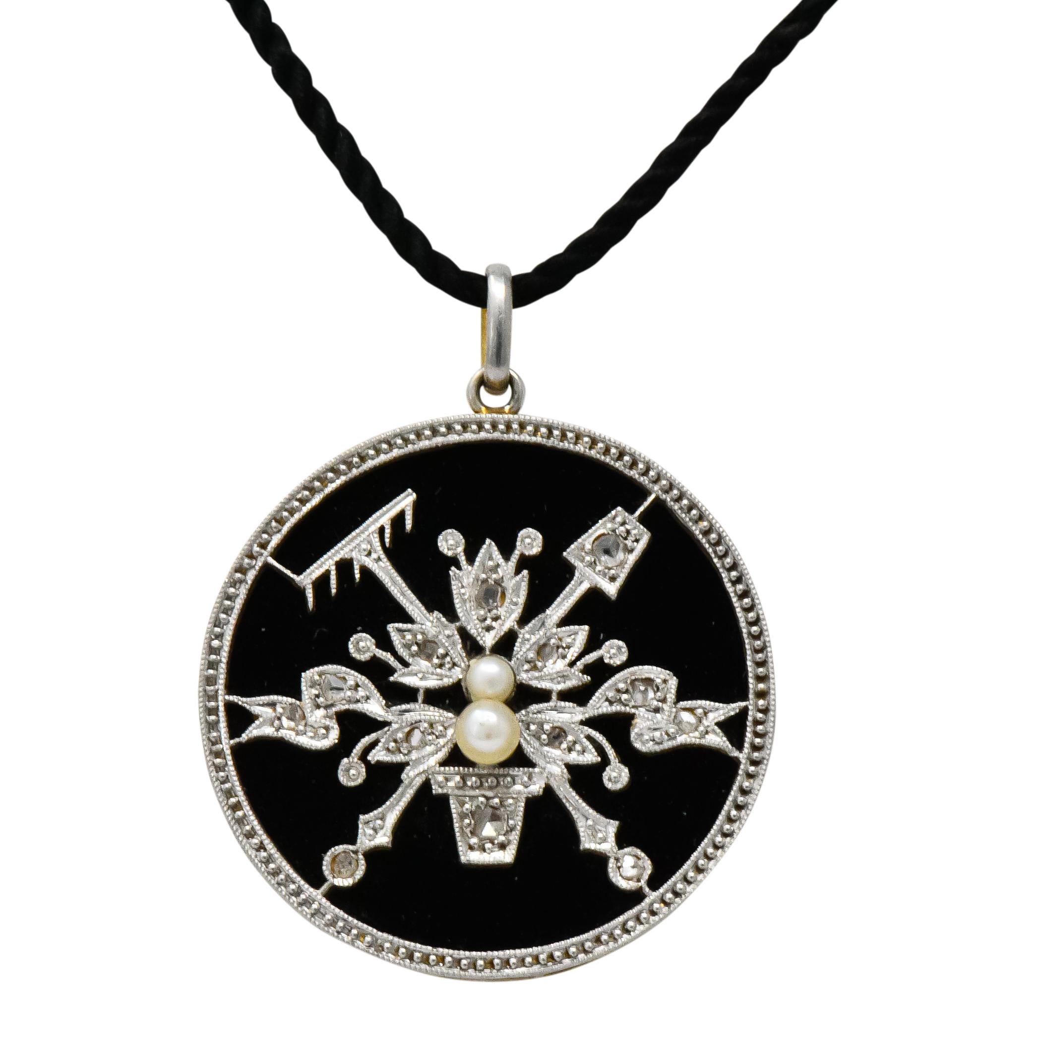 Pendant comprised of onyx inset in platinum-topped, millegrained, circular frame depicting flowers, rake and spade

Bead set through out with rose cut diamonds and accented by two freshwater natural pearls

With platinum-topped bale on cotton cord