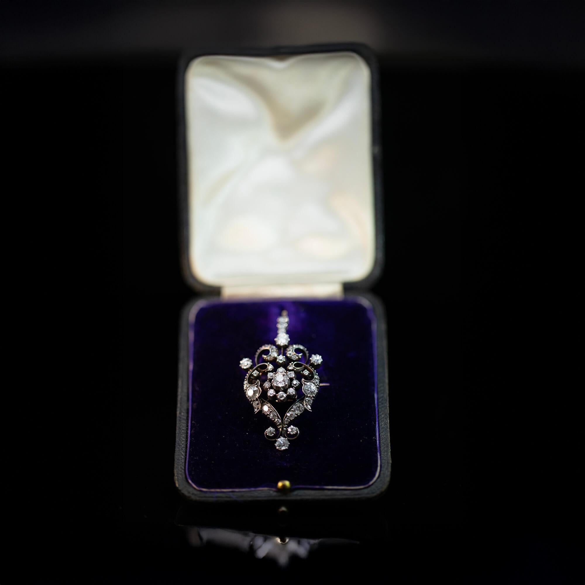 True to the era this Belle Epoque diamond cluster brooch-pendant is hand-crafted with a yellow gold undercarriage and sterling silver settings, featuring old cut diamonds. A central flower cluster is surrounded by scrolls and claw set diamonds. This