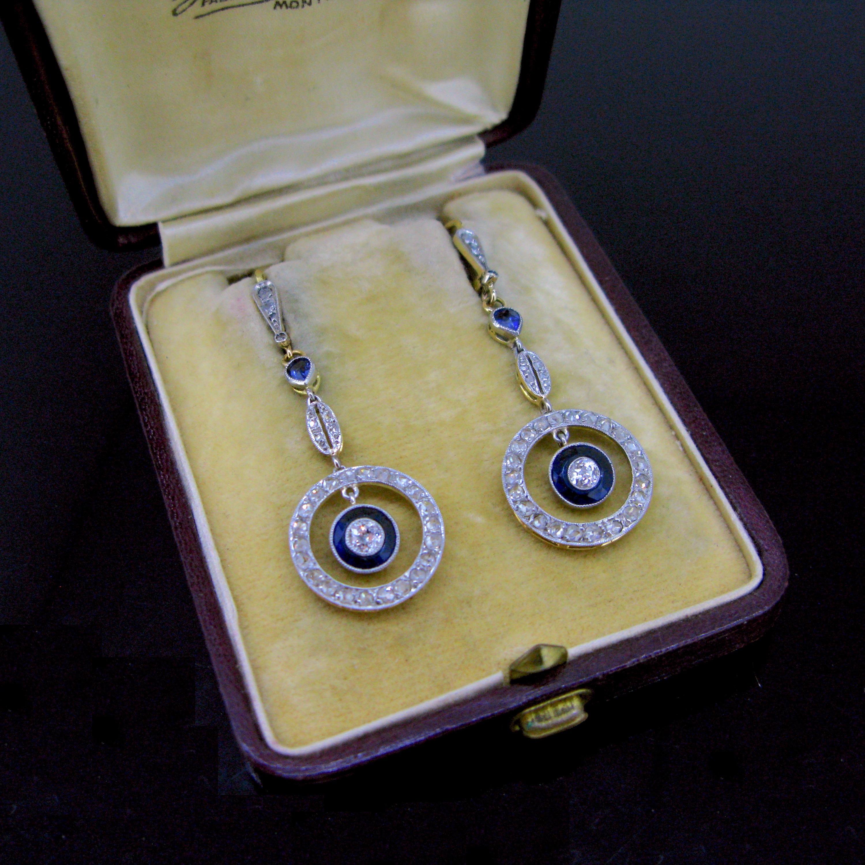This ravishing pair of earrings is from the Belle Epoque era. They are made in 18kt gold and platinum (tested). Each earring is set with an old cut diamond surrounded by a one piece of carved sapphire. The dangling circle on the bottom is set with