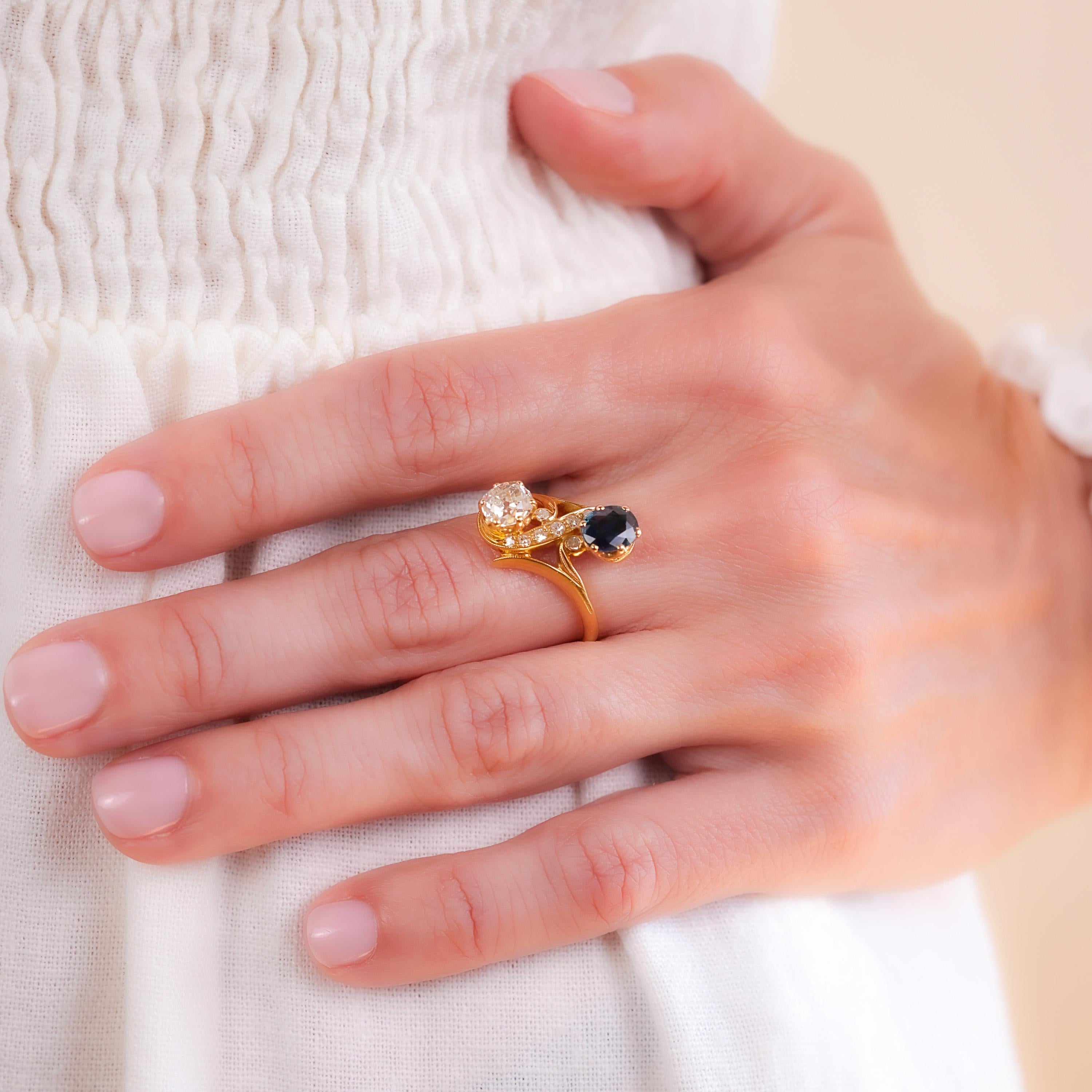 One Belle Époque French Diamond and Sapphire 18k Yellow Gold Toi et Moi Ring. Featuring one old mine cut diamond weighing approximately 1.00 carat, graded I color, VS2 clarity, and one oval mixed cut sapphire weighing approximately 0.90 carat.