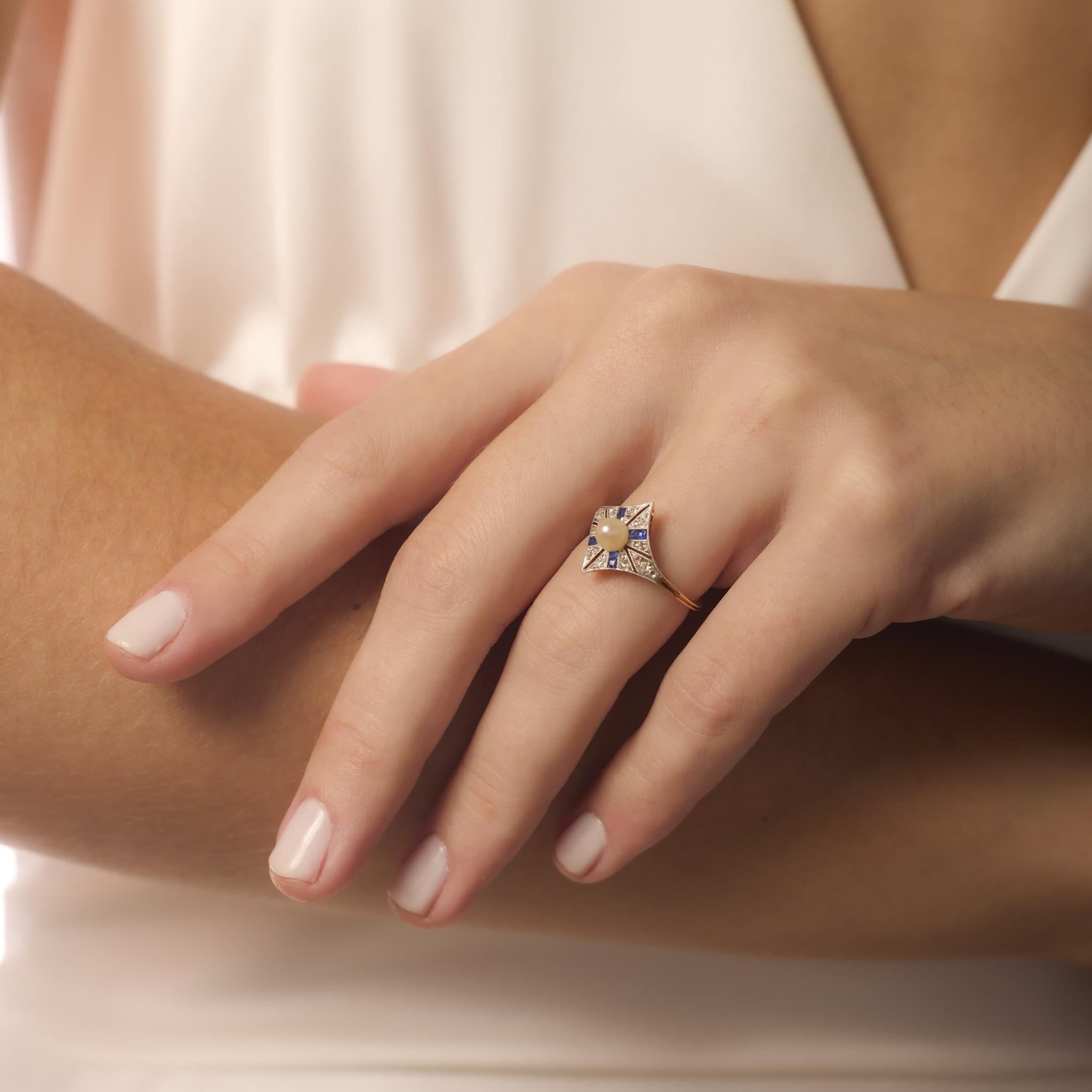 This Belle Époque ring features a luminous pearl framed by blue sapphires and glittering diamonds in an elegant 18k yellow gold and platinum design.