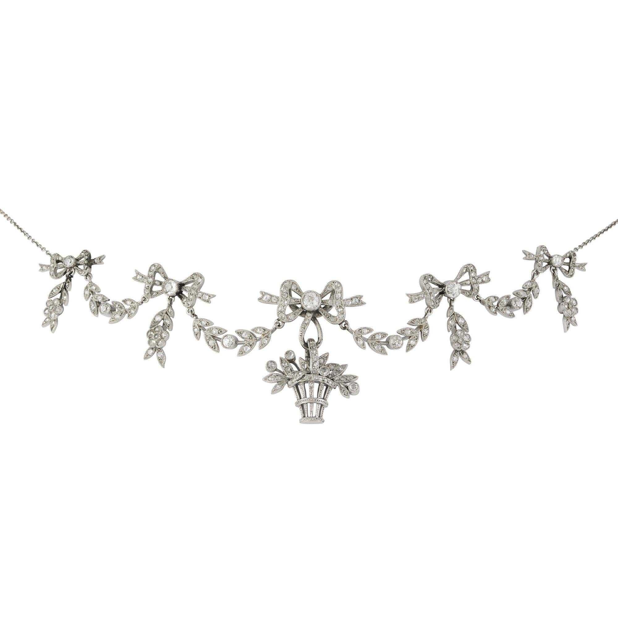 A Belle Epoque diamond necklace, of garland style, centred with a giardinetto motif, articulated beneath a ribbon bow surmount, to graduated swags tied by ribbon bows suspending foliate drops, millegrain set throughout in platinum with old brilliant