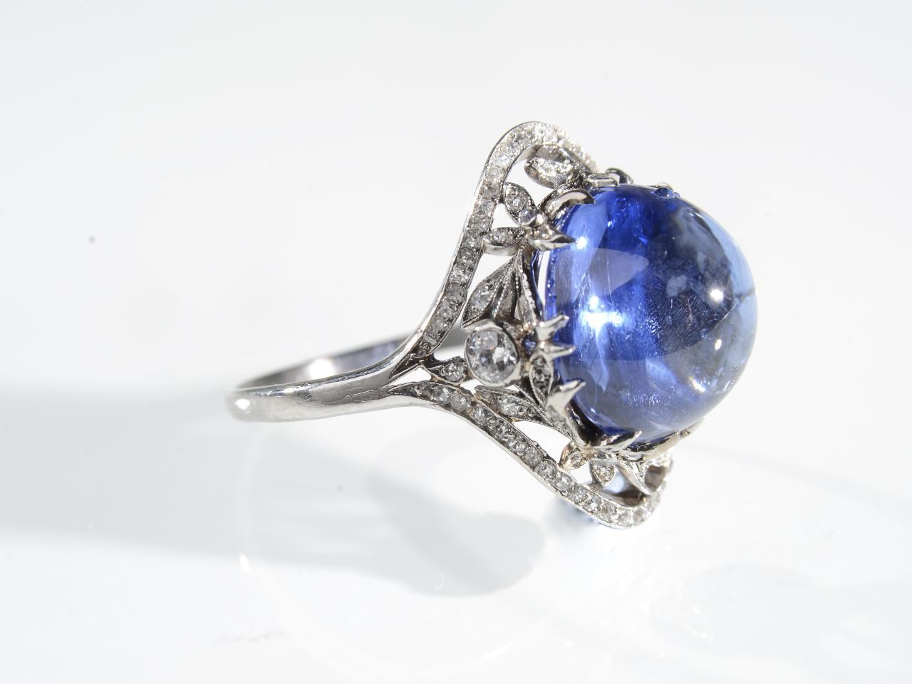 Antique Ceylon sapphire cabochon and diamond ring in platinum, centrally set with a 10.90cts round cabochon Ceylon sapphire, with no indications of heat treatment, in a stylised claw setting, framed by a naturalistic diamond set openwork cluster,
