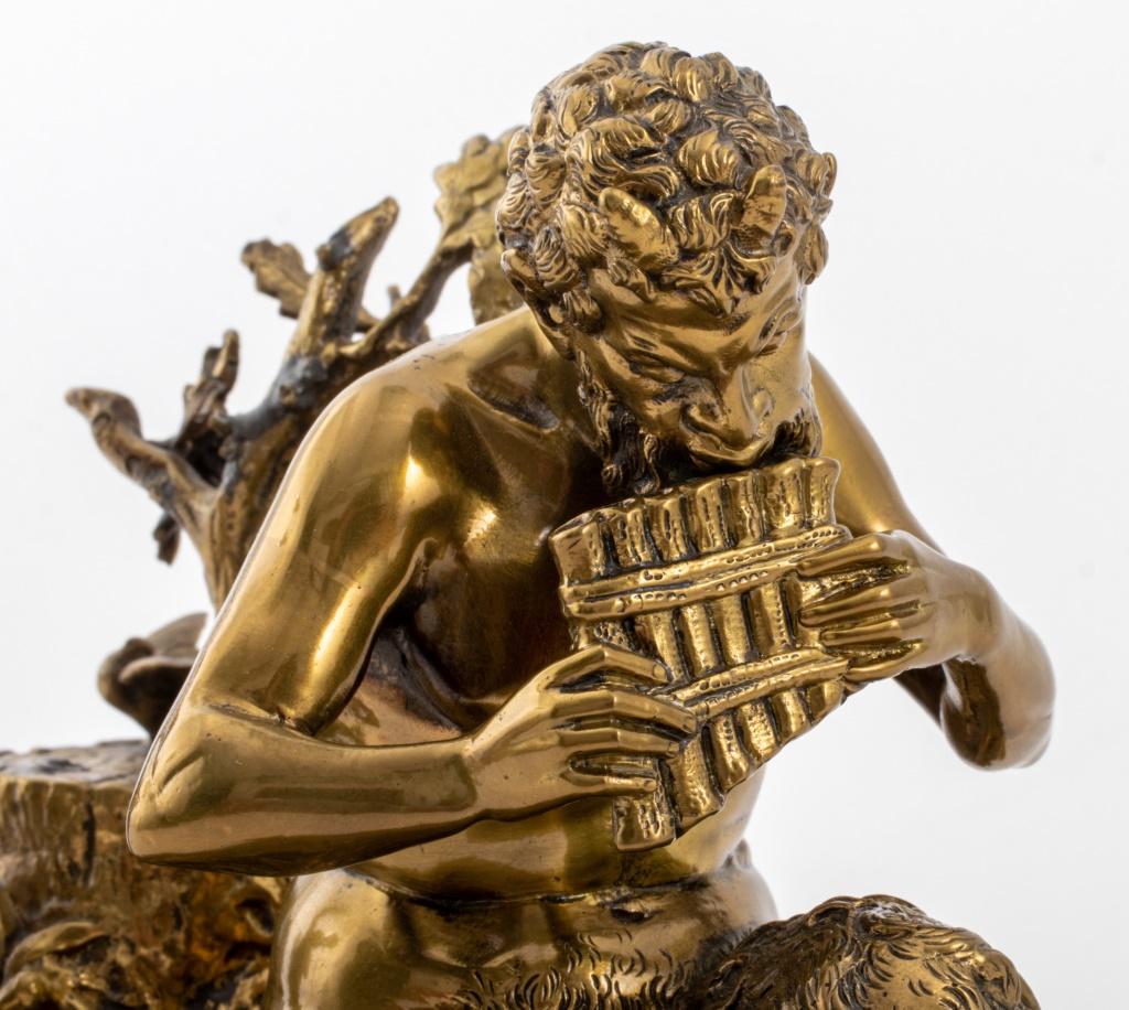 Grupo escultórico de bronce dorado de la Belle Epoque francesa, que representa una figura de Pan tocando la flauta acompañado de dos querubines junto a un tocón de árbol, montado sobre una base foliada con roleos de estilo Luis XV. 5,75