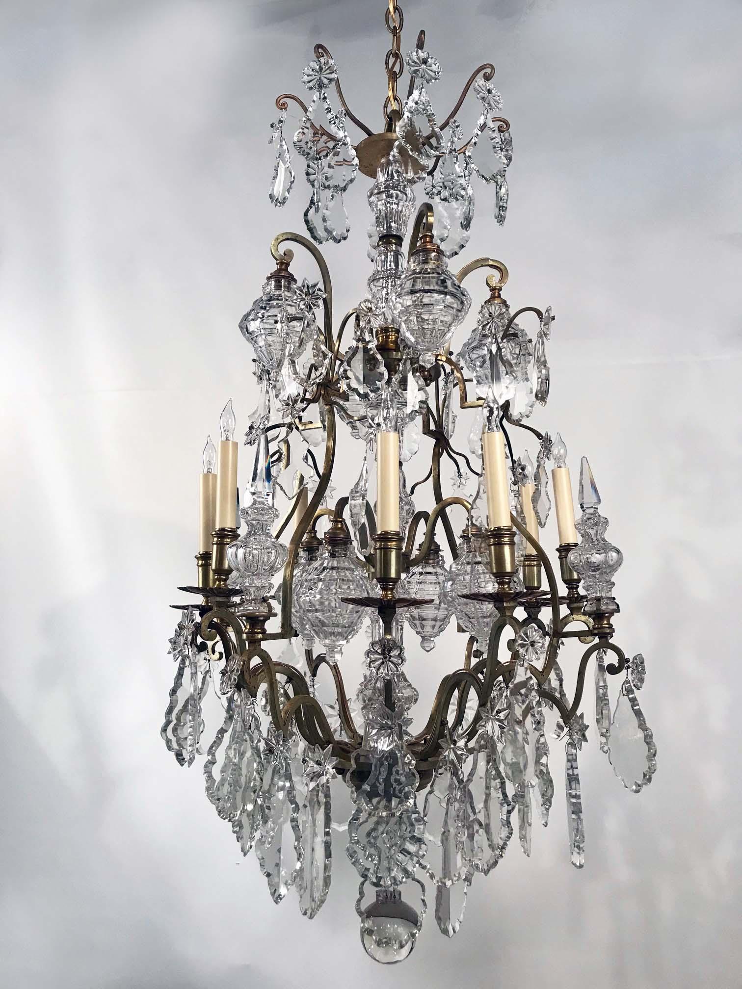 This chandelier has eight candle arms and most unusually eight further lights enclosed in faceted shades. This dates it to a time when electric lighting was less intense; we think the Belle Époque. It is boldly hung with large violin pendents, star