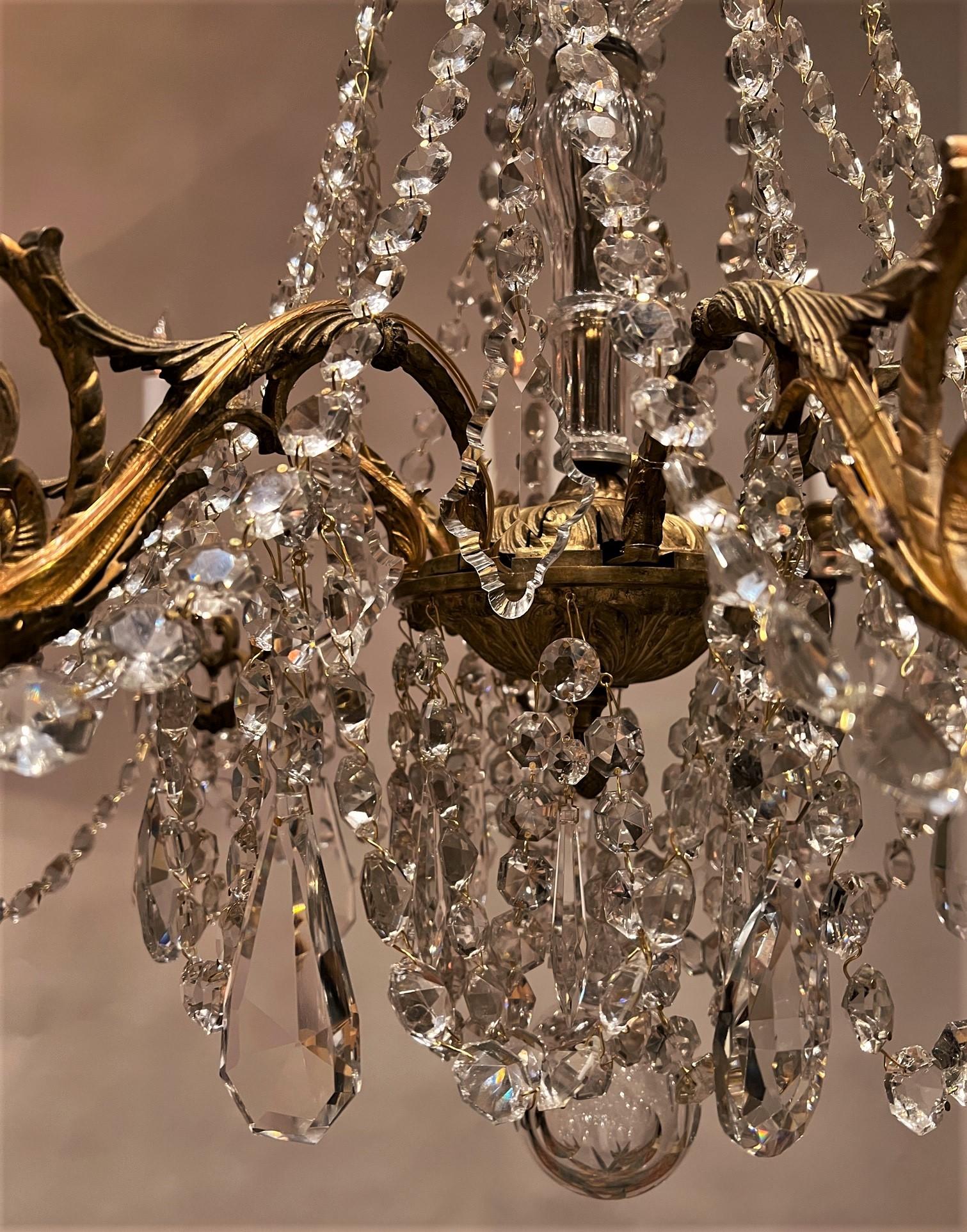 This beautiful Belle Epoque chandelier has a hand-cast gilt brass frame & hand-cut crystal prisms. It was originally a candle fixture that was not electrified until the 1930's and has now been newly re-wired. Baccarat style prisms adorn the