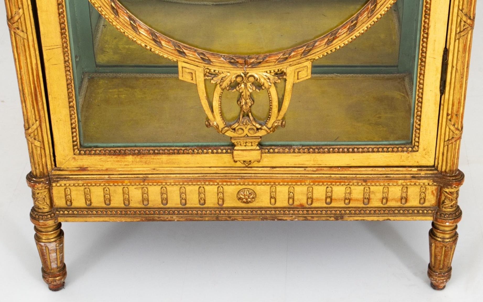 Belle Epoque Louis XVI style gilt wood vitrine, circa 1890s, with shaped rectangular top centering a floral cartouche, the glazed door and sides flanked by ribbon-tied fluted colonnettes, the door with ribbon-wrapped and beaded oval molding with