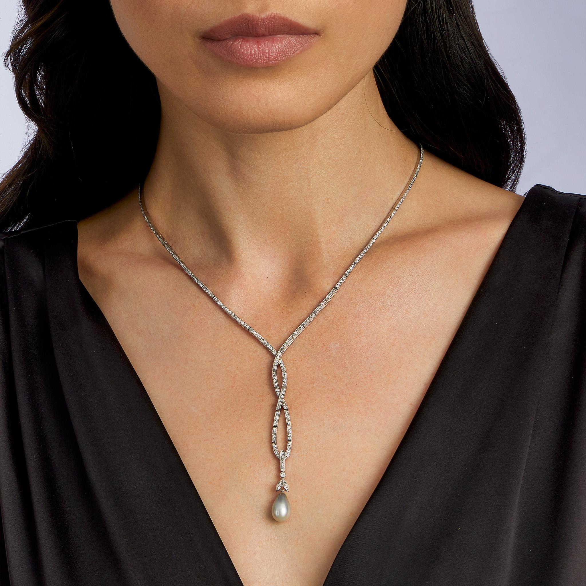 Dieses deutsche Lavalier-Collier aus Platin, besetzt mit Diamanten und einer Naturperle, stammt aus der Zeit um 1910. Er ist als schmales, sich kreuzendes Band aus rosafarbenen Diamanten, Diamanten im alten Einheitsschliff und Diamanten im alten
