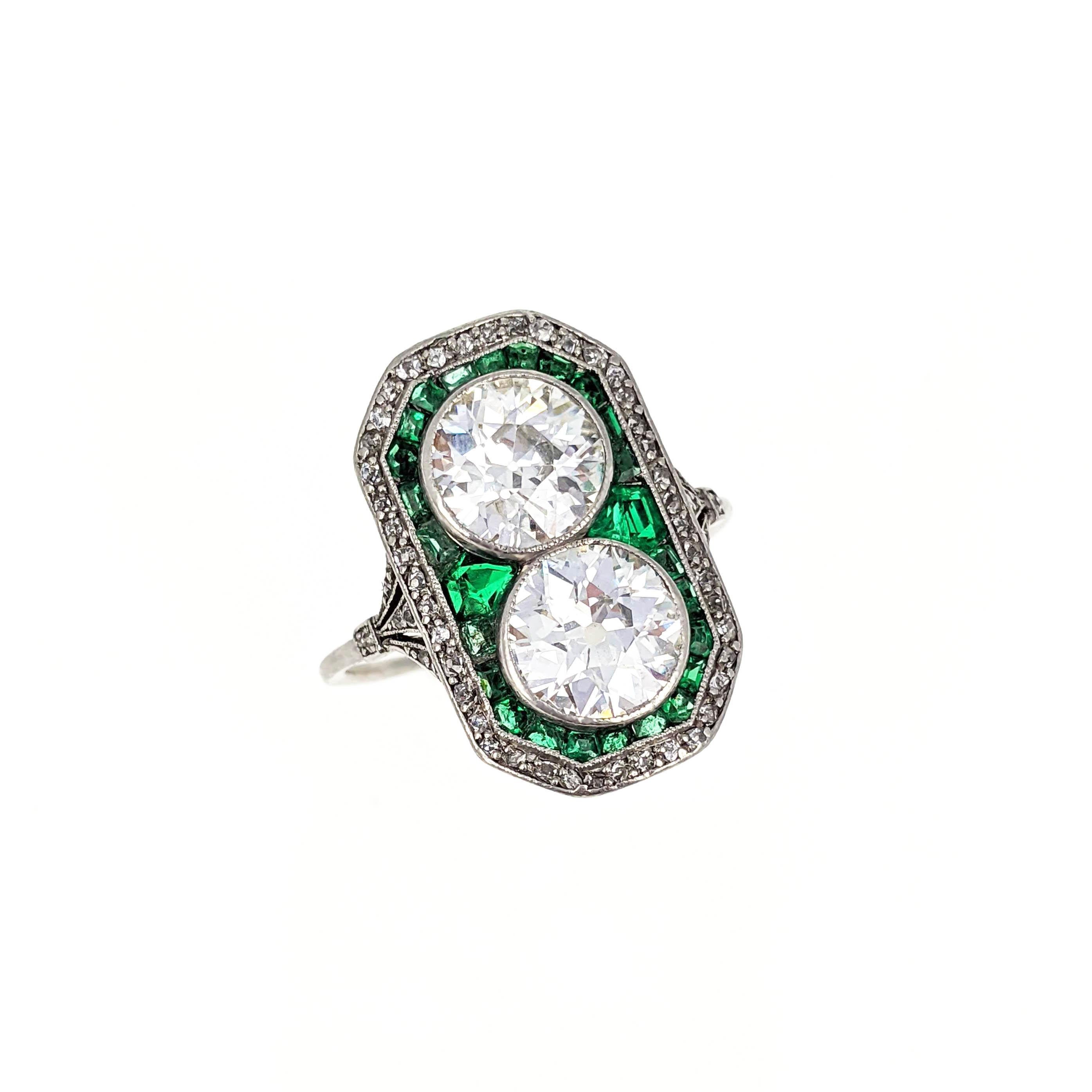 This beautiful Belle Epoque ring features two old European-cut diamonds weighing approximately 3 carats total. They are surrounded by calibre-cut emeralds with a border of rose-cut diamonds. The ring is mounted in platinum with French assay mark.