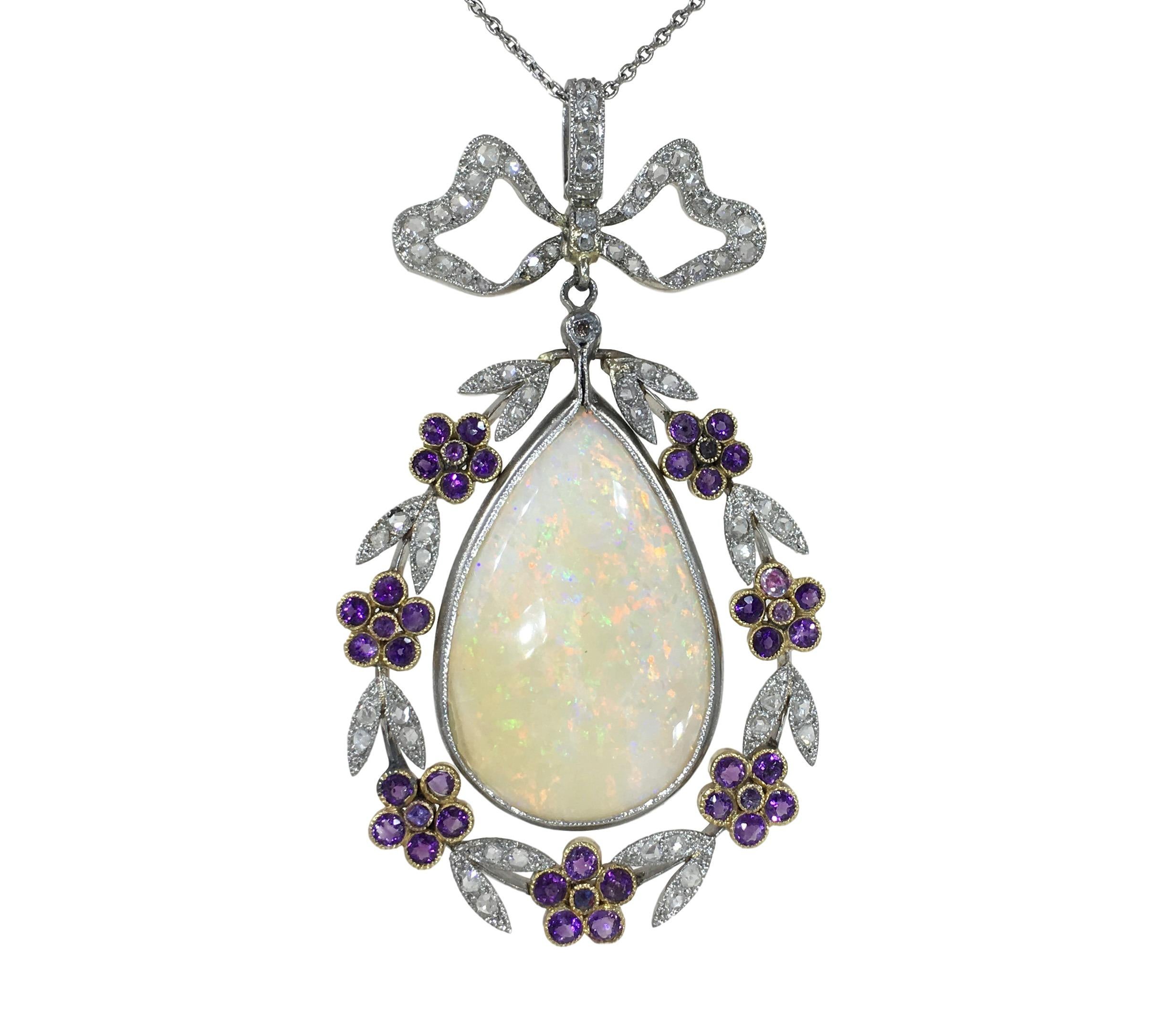 A delightfully pretty pendant centering on a pear-shaped cabochon of white opal with good play of colour ranging from vivid reds and oranges through to hints of green and violet. The opal is set in a platinum mount and suspended within a garland