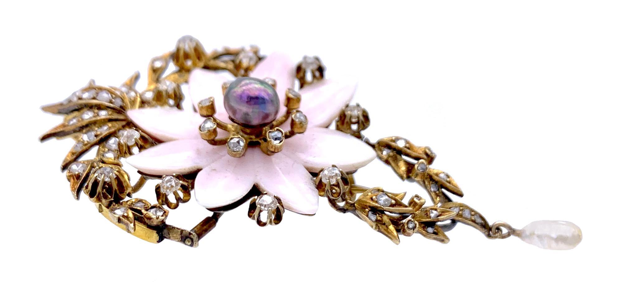 This elegant Belle Époque jewel was created out of 14 karat gold and can be worn as a pendant or a brooch. A natural black oriental pearl surrounded by diamond set pistils, delicate flower leaves carved out of pink shell and diamond set flower buds