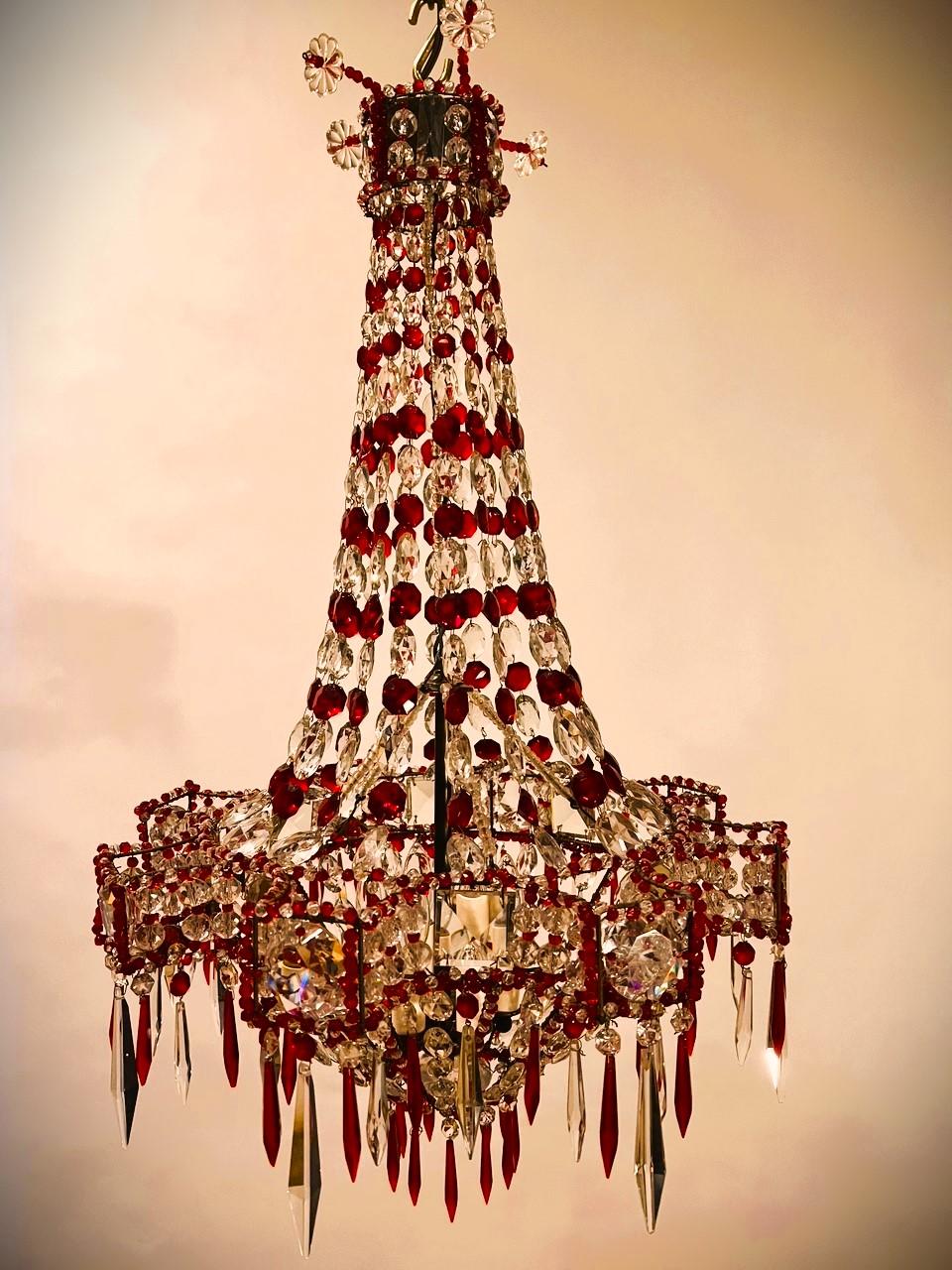 This is a truly stunning fixture. The combination of clear and rich red Baccarat prisms with its Empire shape make it remarkable. The chandelier has 6 lights clustered inside the bottom bell. The frame is brass with a wide variety of bead, button,
