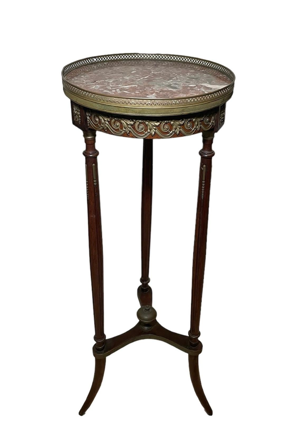 This is a Belle Epoque style Wood and Marble Plant Stand/Table. It depicts a round brown-grey marble top adorned with a gilt brass gallery. The marble is supported by a round dark wood base enhanced by brass made scrolls of acanthus leaves and