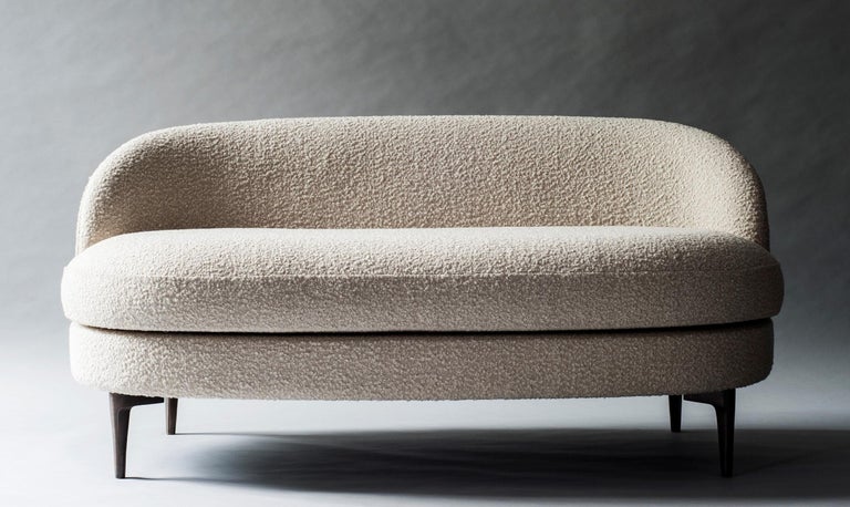 The elliptical seat of the Belle sofa or settee rests upon a bronze frame that turns structure into a defining element of design. The sofa’s rounded back and loose seat cushion provide soft curves against the angular frame.