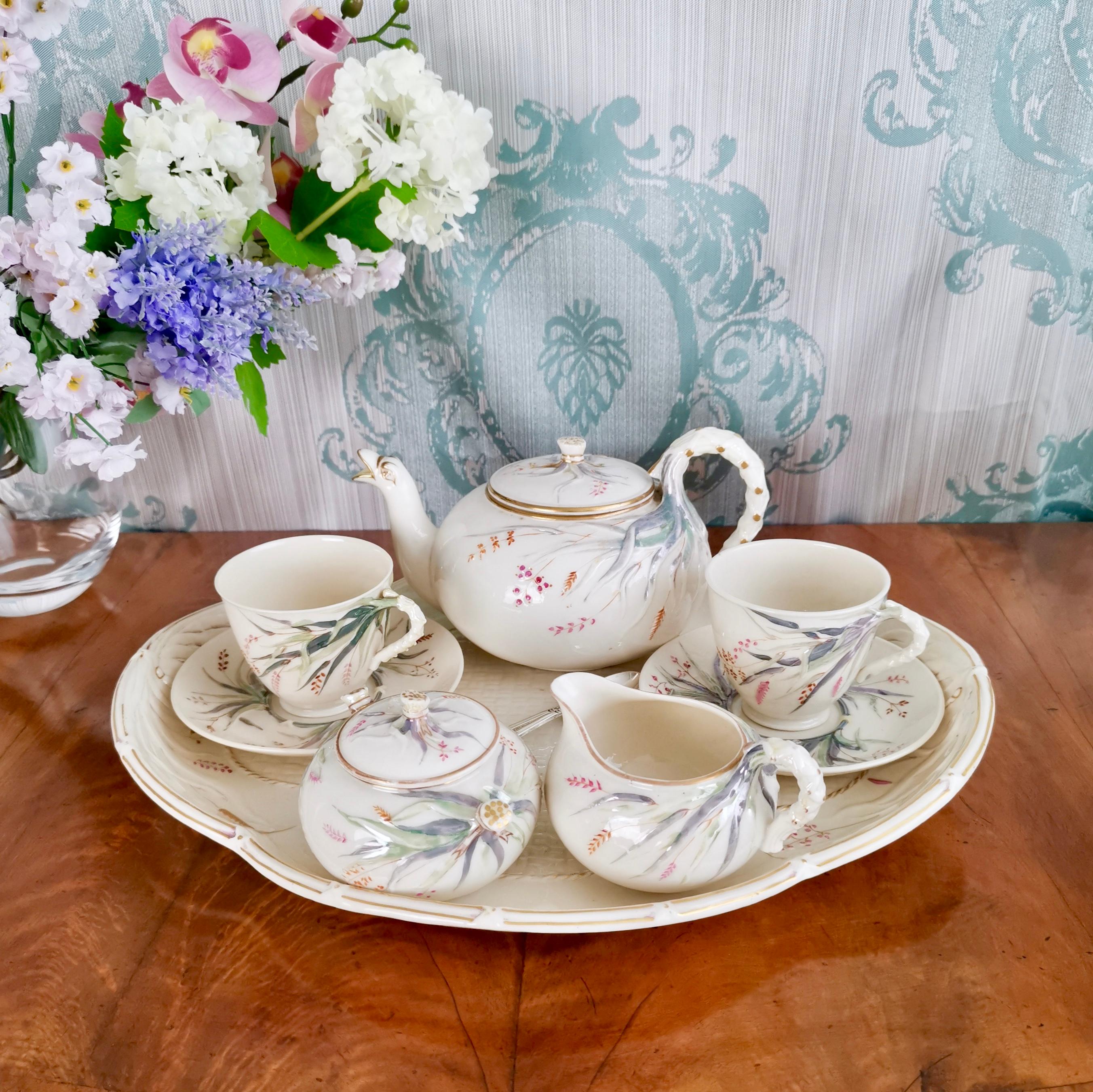 This is a beautiful Belleek porcelain cabaret tea set in the Grass design made by Belleek between 1863 and 1891, which was the Victorian era. It consists of a teapot, two teacups and saucers, a milk jug and a lidded sugar bowl, all placed on a large