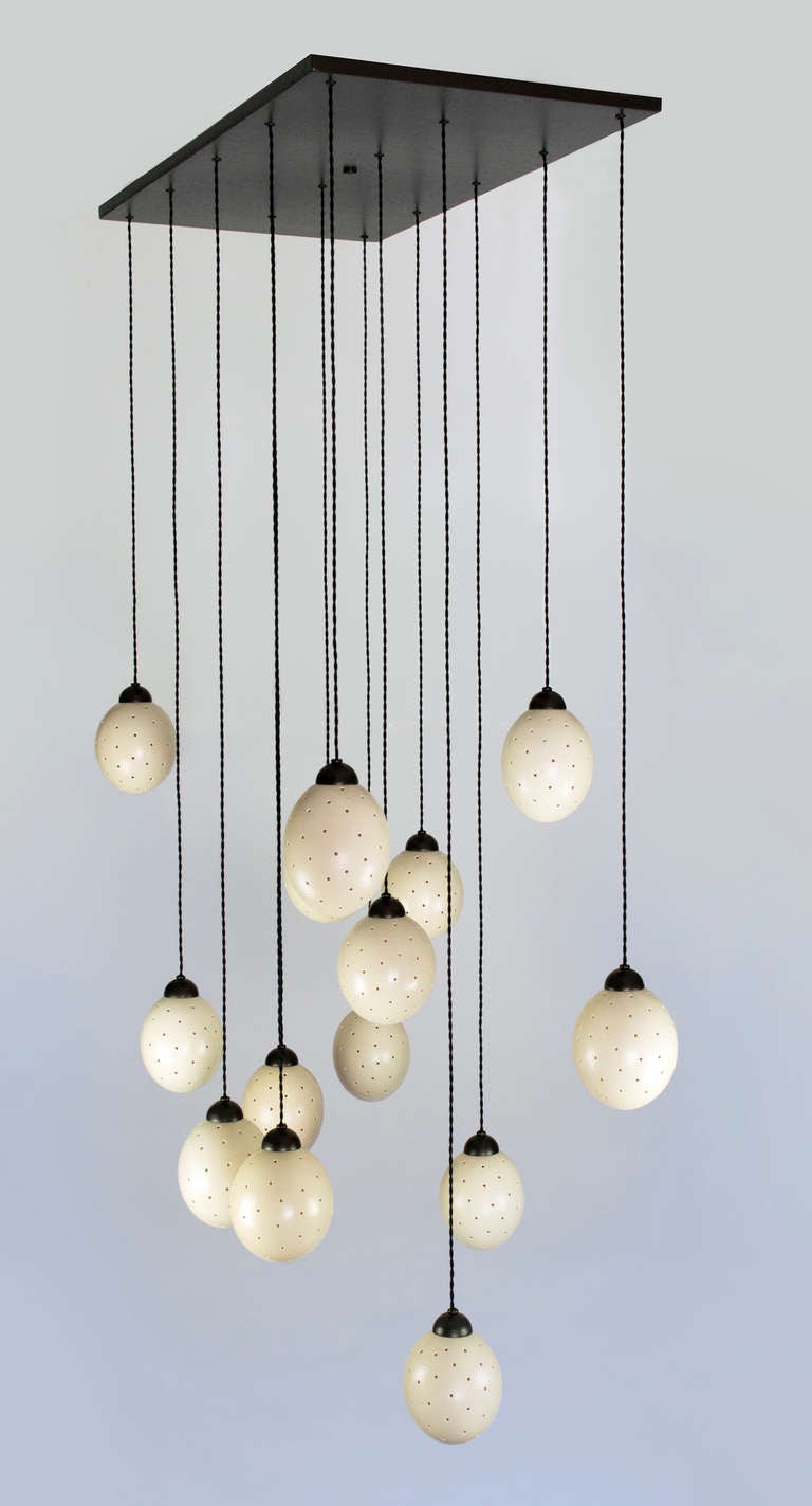14 œufs d'autruche percés suspendus à un baldaquin en bronze. Fils de soie tressés.
Le luminaire utilise des ampoules à culot candélabre.
25 watts max. pour les œufs d'autruche
La hauteur peut être ajustée sur place.