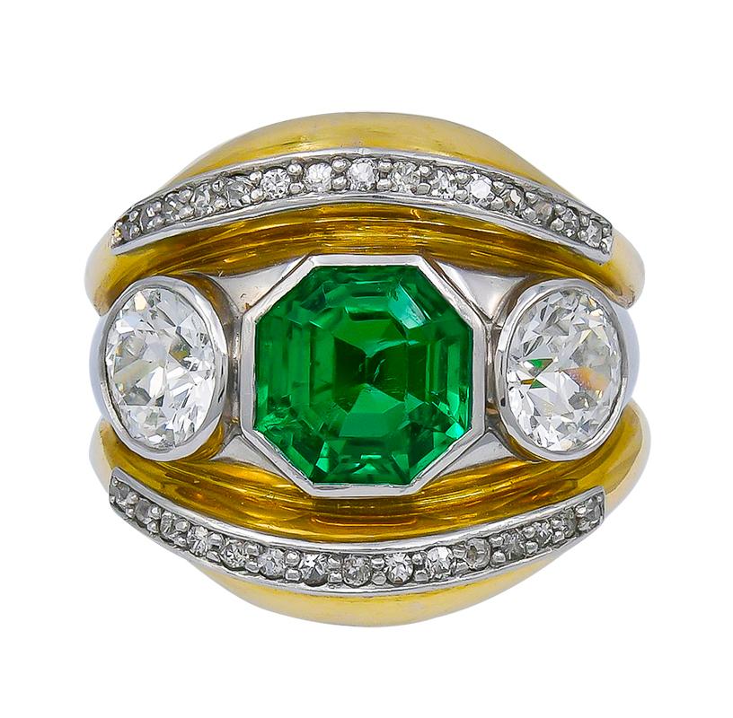 The bold 18kt yellow gold ring centering three stones set horizontally, an octagonal-cut emerald weighing app. 2.50 carats flanked by two old European-cut diamonds weighing app. 1.95 carats total, all bezel-set in platinum, enhanced above and below