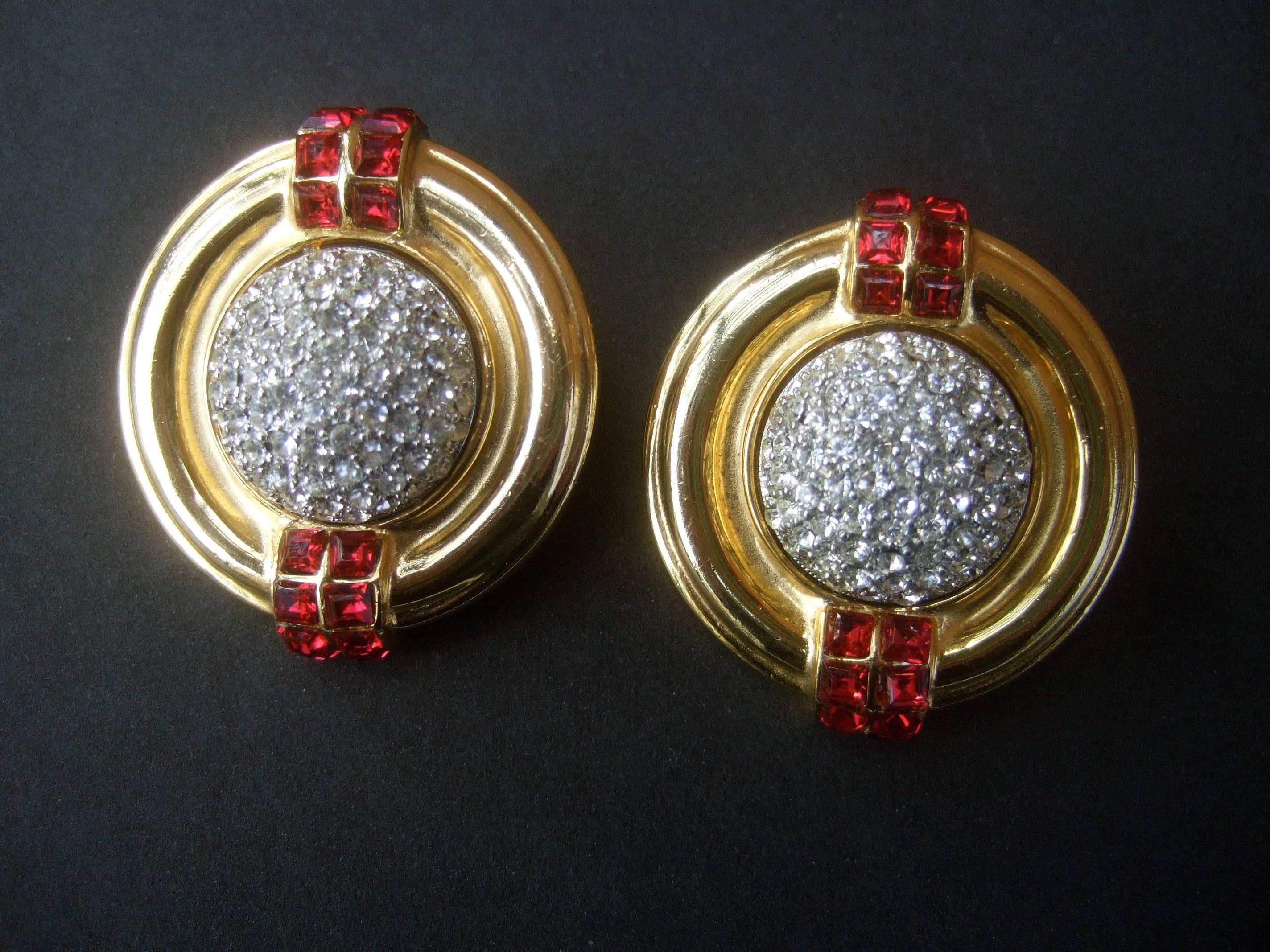 Ben Amun Elegant crystal encrusted art deco style clip earrings c 1980s
The stylish clip on designer earrings are encrusted with a dome
of glittering pave crystals 

The shiny gilt metal edges are embellished with two rows 
of ruby color glass