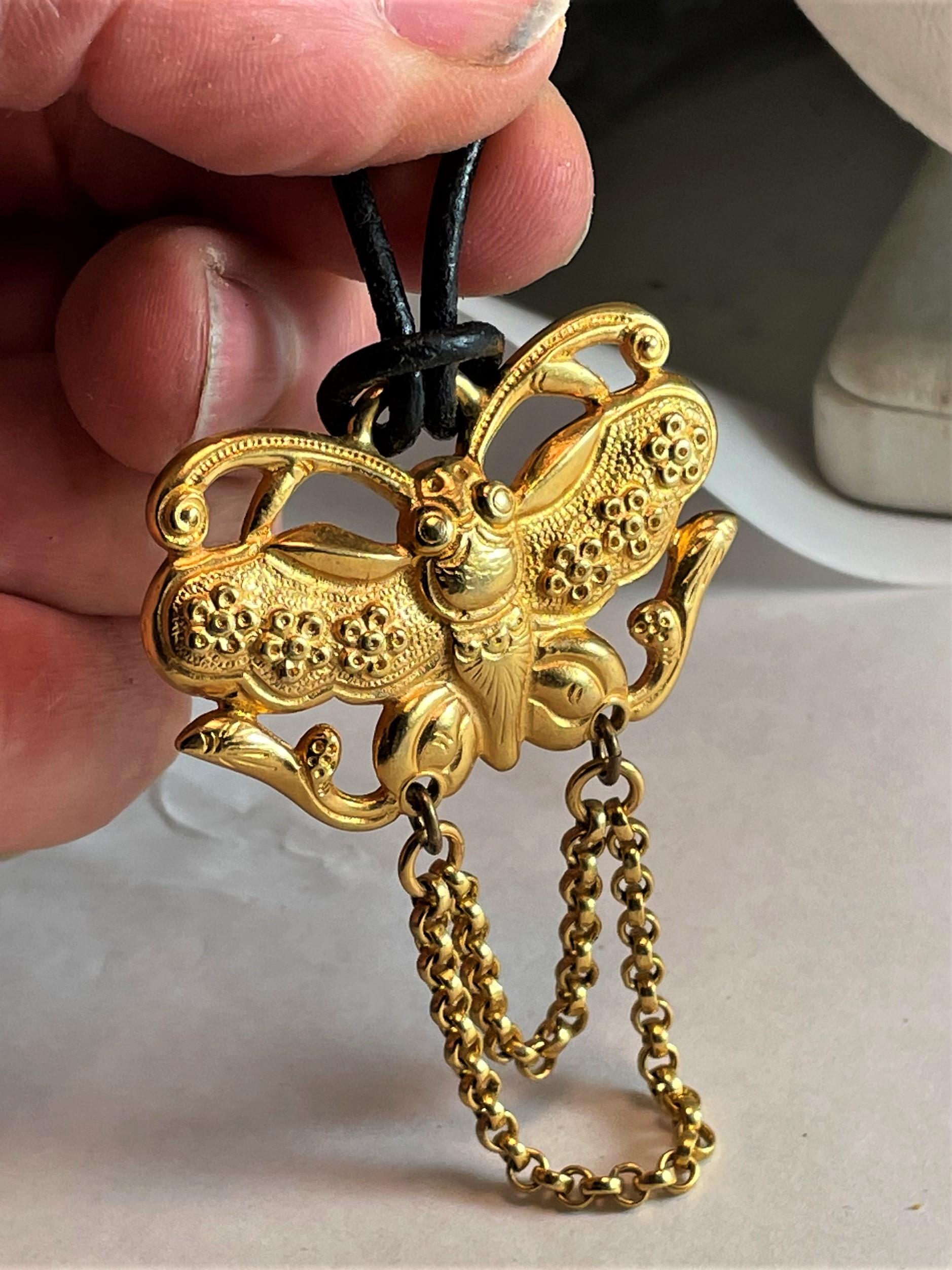 What an exotic bright gold pendant of a fancy butterfly with exaggerated antenna 0n the top and legs on the bottom. There are raised flowers on the wings, a beetle head and eyes and a double strand rolo chain dangling below, giving it a mythical