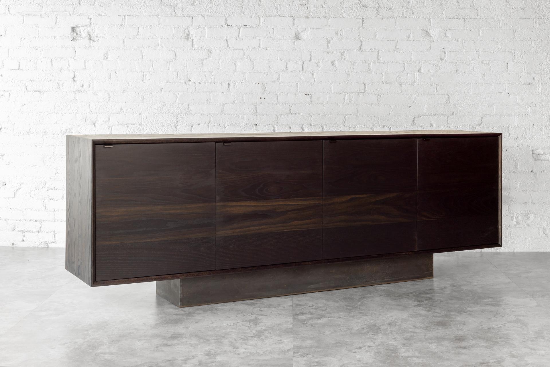 Solid blackened oak credenza constructed with uncommonly practiced solid wood carcass, cabinet doors, and interior shelves. Four cabinet doors, with interior shelves. Black steel door pulls, soft close hinges set on a blackened steel base for