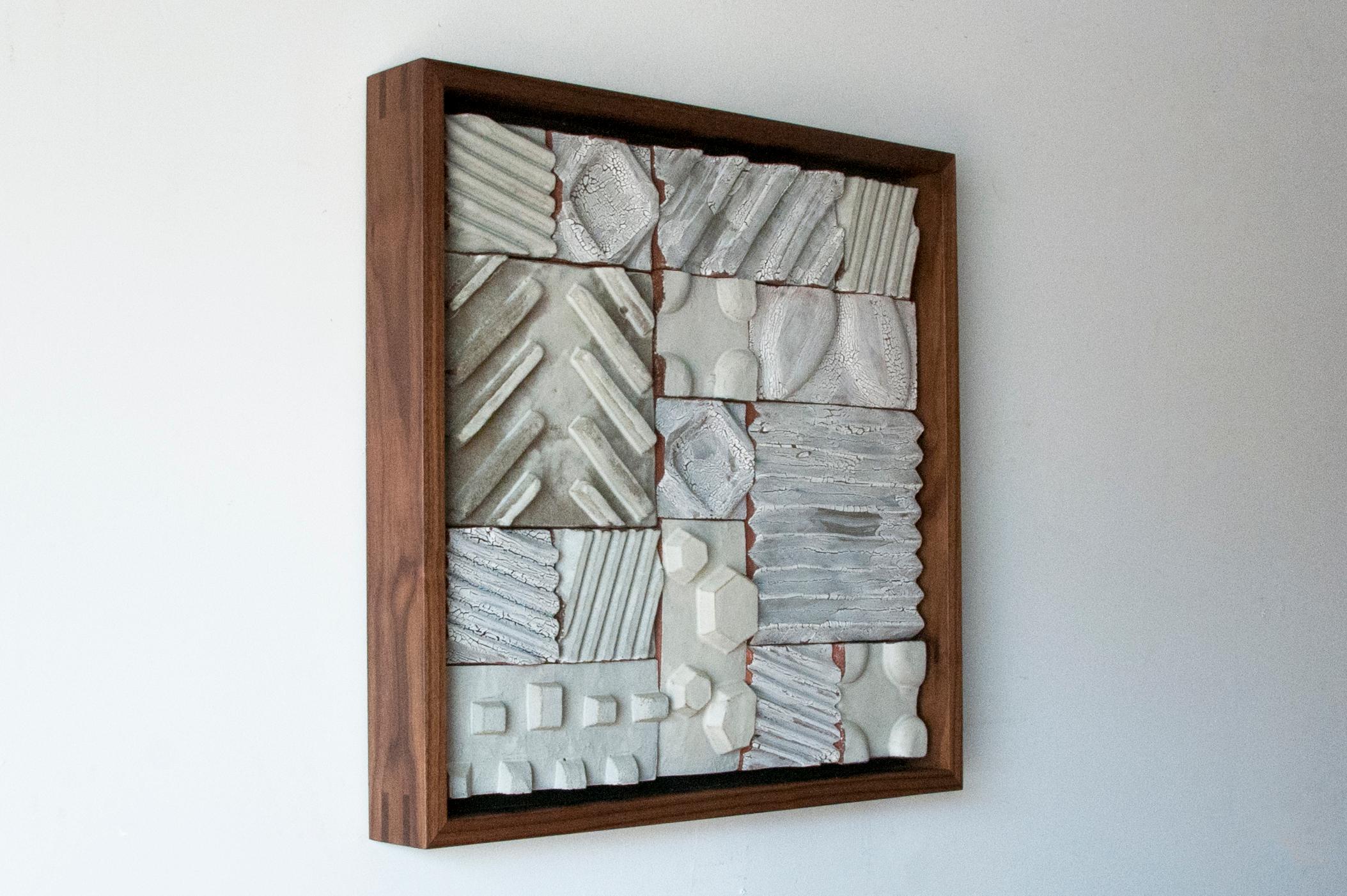 This minimalist ceramic wall sculpture is a beautiful handmade piece by American artist Ben Medansky, which includes a walnut wood frame. This wooden framed wall sculpture is made of neutral colored terracotta tiles covered in a textured glaze,