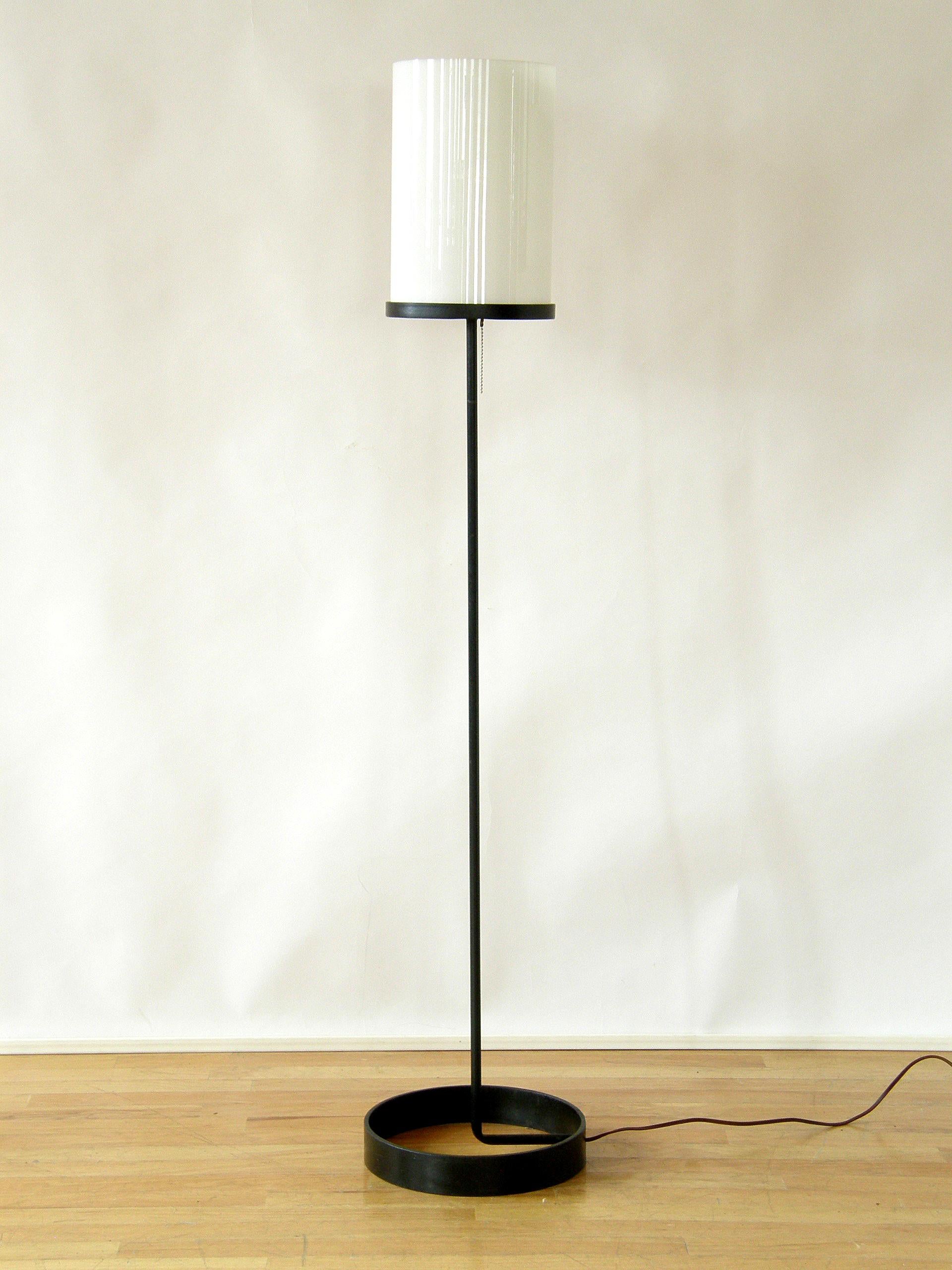 This Minimalist, Mid-Century Modern floor lamp was designed by Ben Seibel for Raymor. It has an iron frame with a black finish and a circular base and shade support. The shade is a white glass cylinder.

Please note that the shade was replaced by