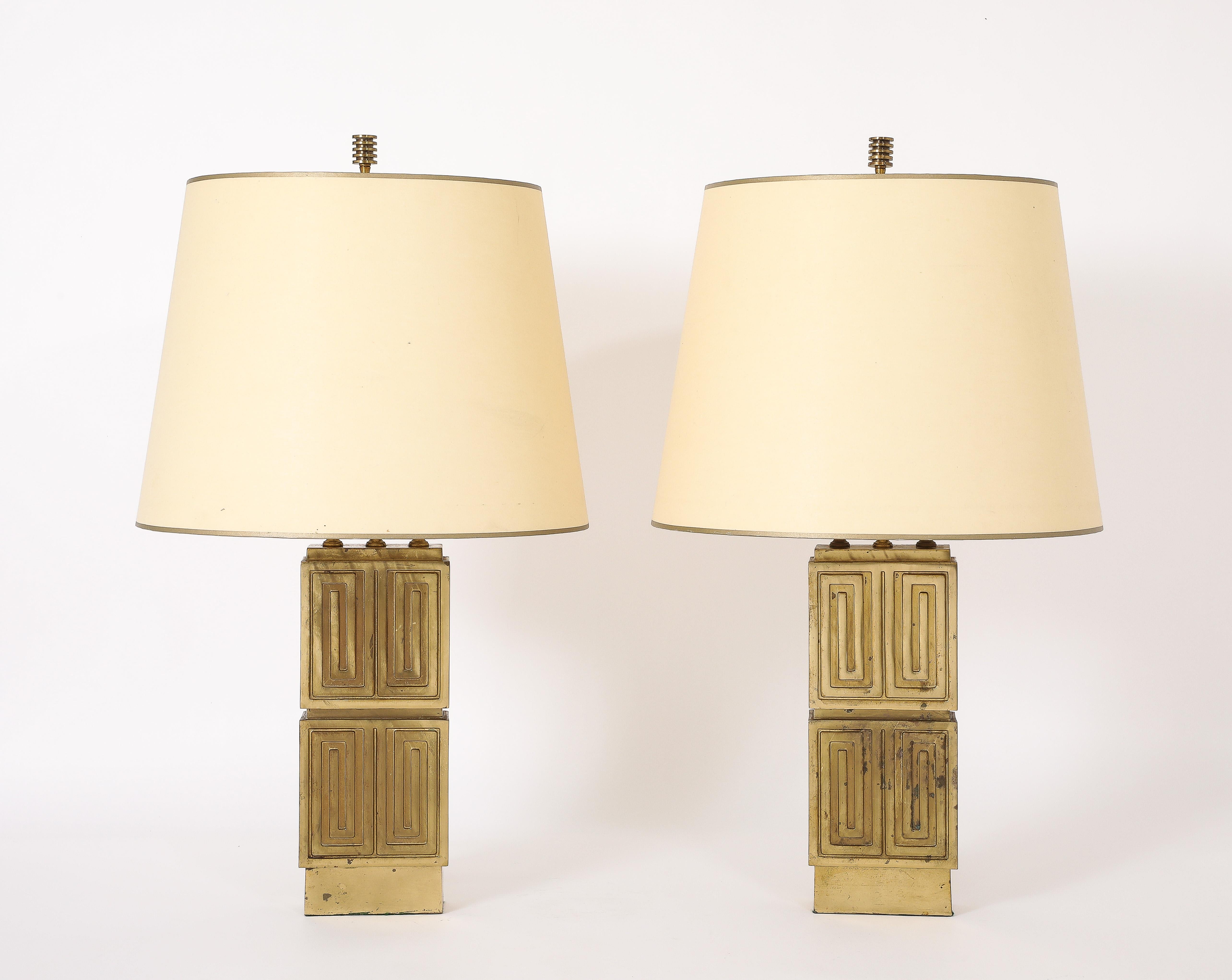 Coppia di grandi lampade in ottone con motivi concentrici su una base a gradini con terminali originali e patina. Le tonalità sono vintage.