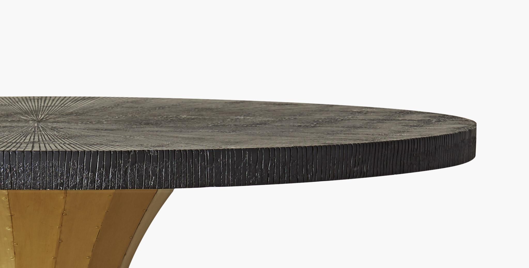 The gleaming curved brass paneled pedestal of the Raine dining table is elegantly contrasted with a generous round blackened table top with a subtle sunburst pattern.
  