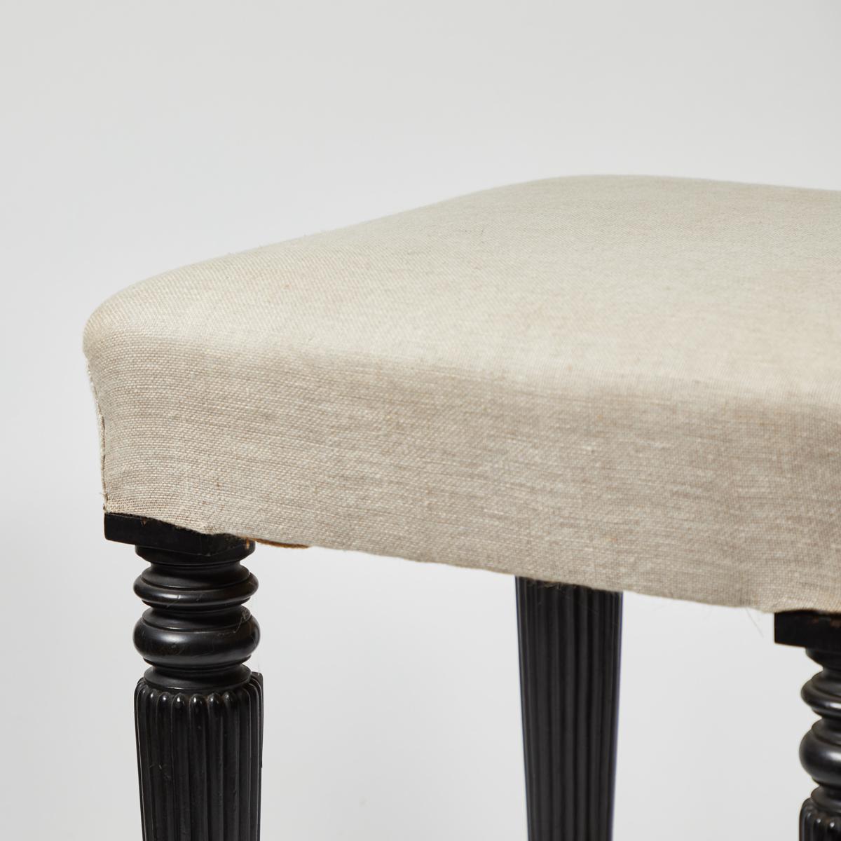Late 19th-century English stool with fluted and turned ebonized wood legs, reupholstered in a beautiful flax-toned linen. Versatile and with charming proportioned, this stool adds a classic, understated touch to any space. 

England, circa