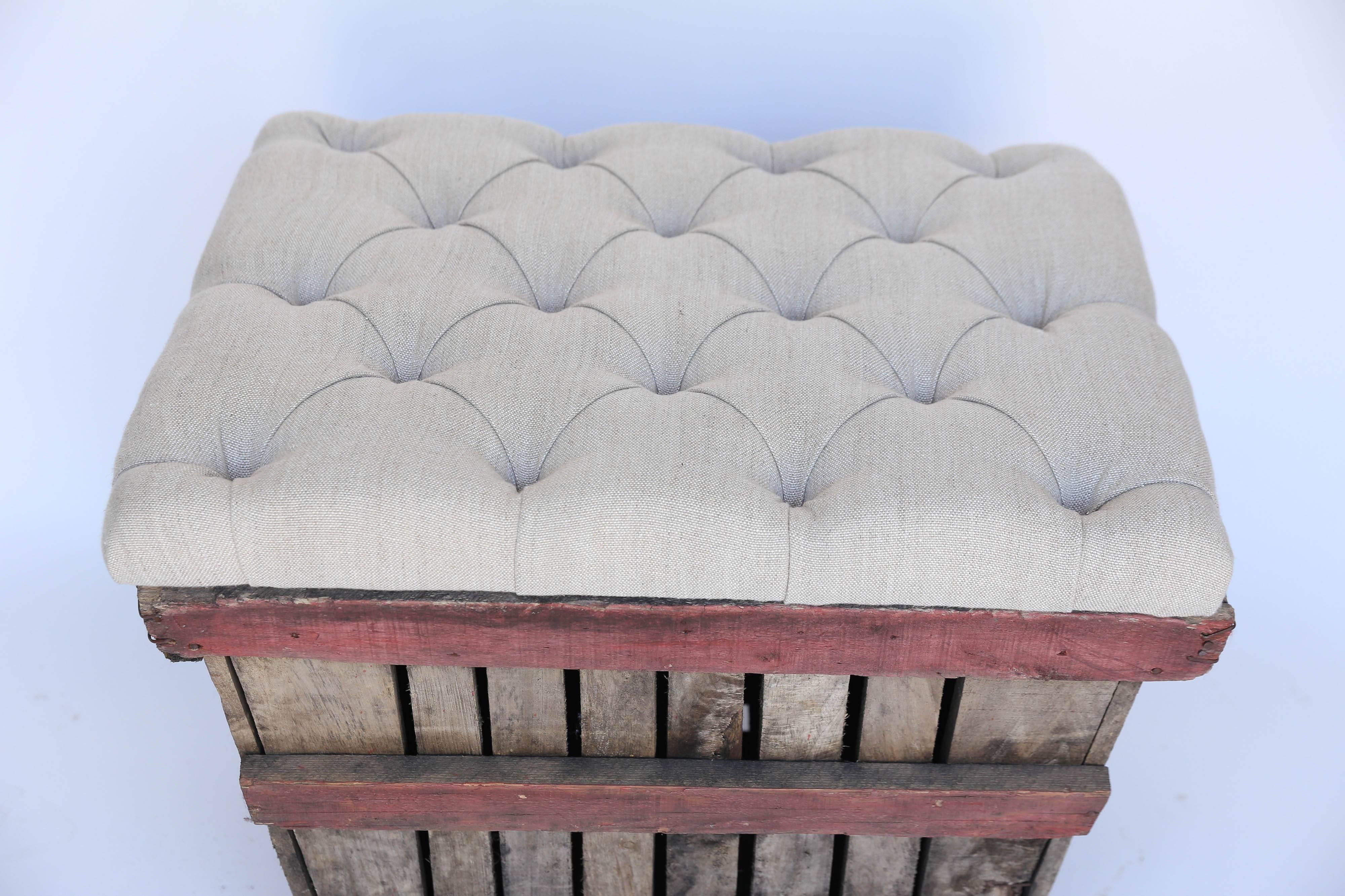 A old grape crate becomes a wonderful bench with the addition of an attached cushion of tufted linen. Tufted with covered buttons, the dressy linen top is in contrast to the rustic wooden bottom. The top is hinged and the interior affords room for