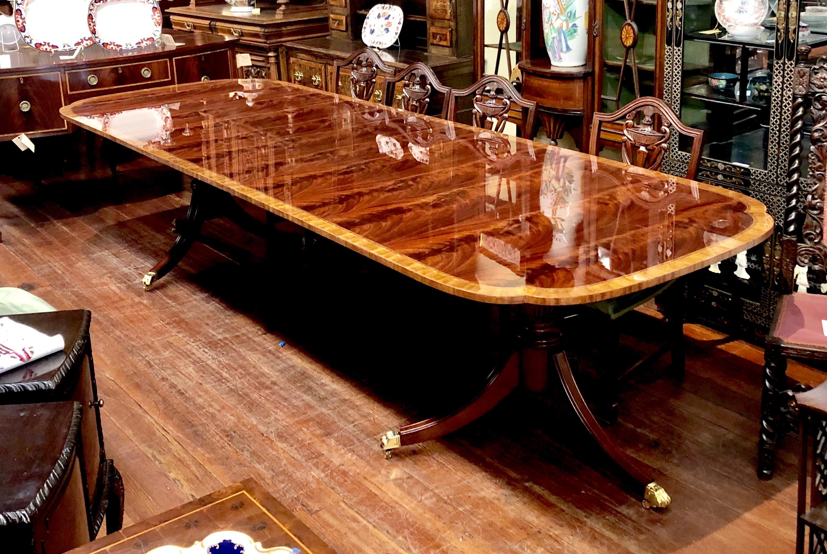 Fabulous quality domestically bench made reproduction inlaid and book-matched flame or crotch mahogany Sheraton style two pedestal, three leaf scalloped corner dining table with fabulous satinwood crossbanded border and narrow inner rosewood inlaid