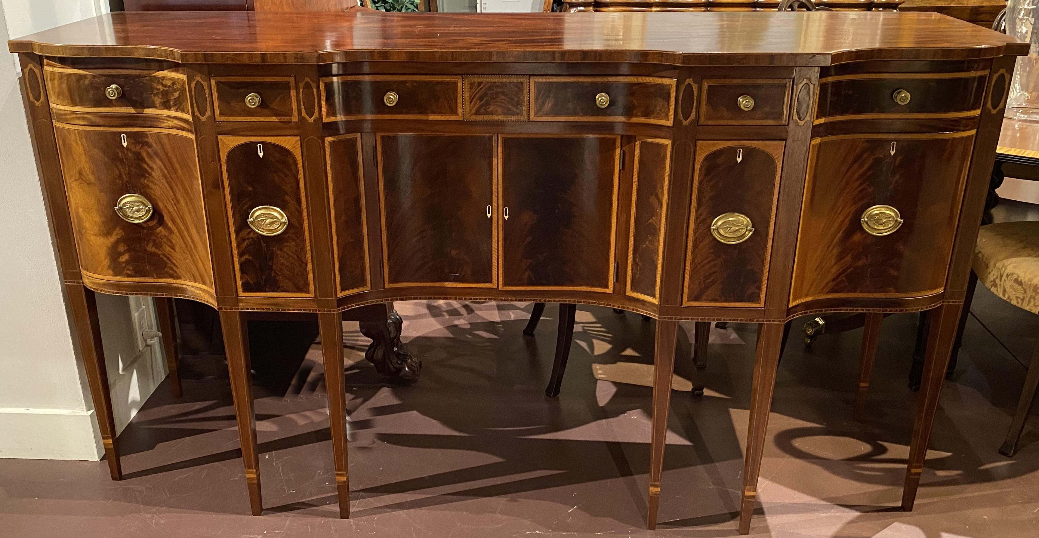 A fine example of a bench made mahogany Federal style sideboard with shaped top surmounting a conforming case with five fitted frieze drawers, each with cross banded veneer borders and round punched brass pulls, over a central two door storage