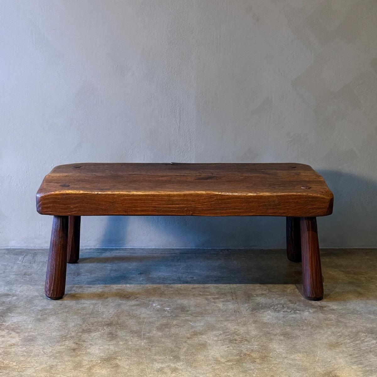 Questo tavolino o panca versatile, realizzato in legno massiccio e con una superficie ricca di texture, incarna le qualità organiche e scultoree del design belga di metà secolo. Le gambe spesse e arrotondate garantiscono stabilità, mentre i bordi