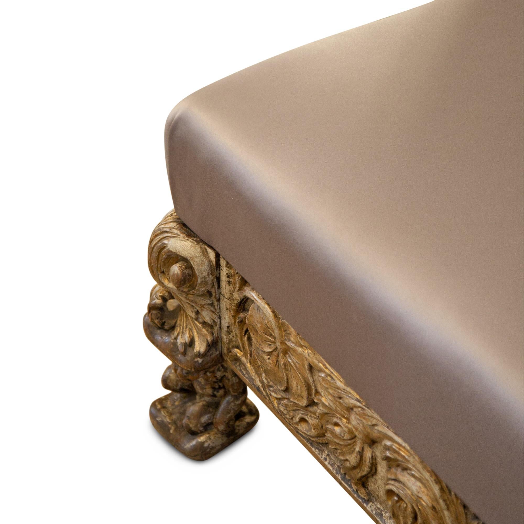 Bench with carved flowers and leaves on three sides. It is in an original condition with traces of the old gilding. The feet are caryatid putti. Newly upholstered with a high quality satin fabric in a beautiful taupe color. Measures: Height of the