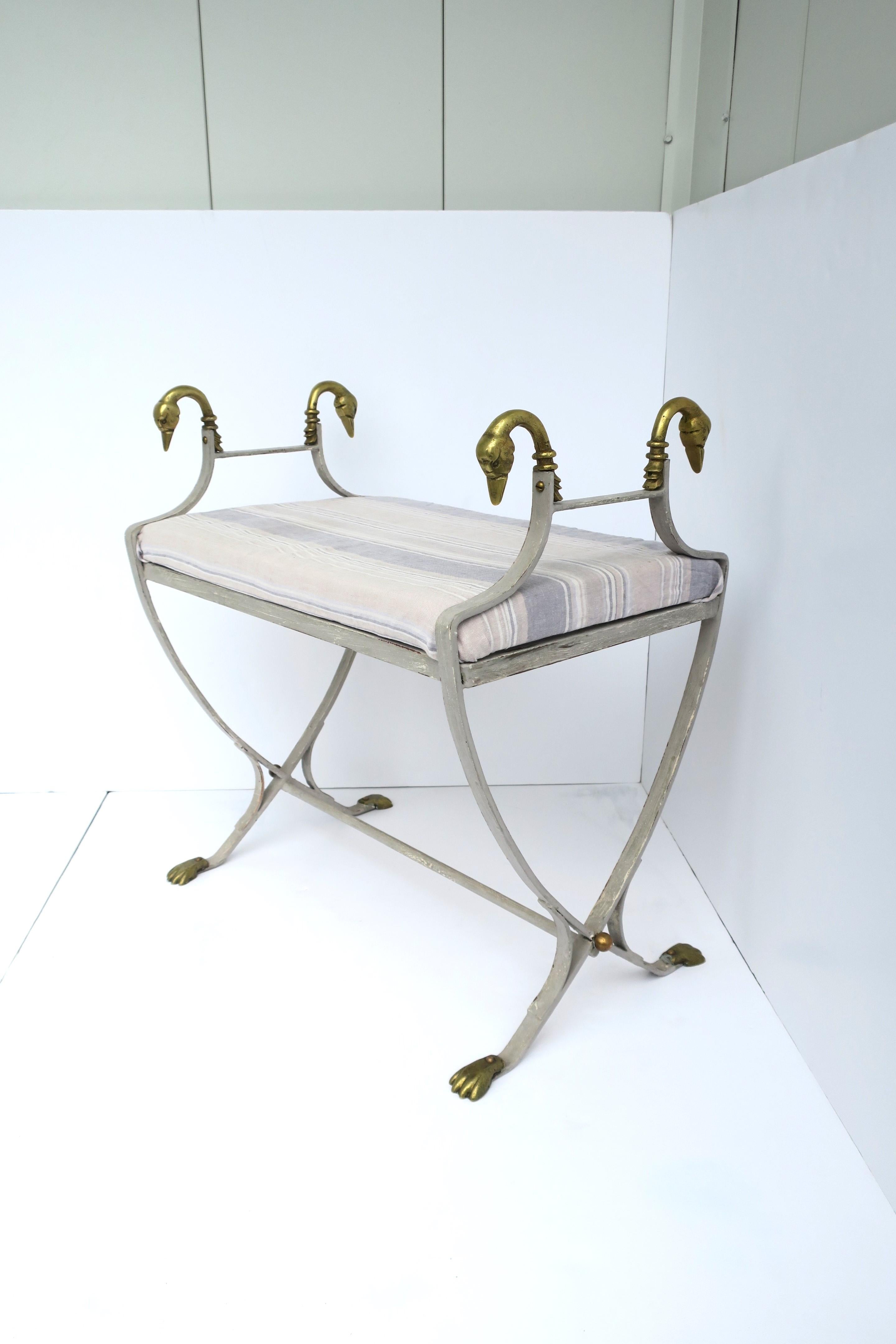 A beautiful grey metal framed and brass swan bird head bench in the Regency style, circa mid-20th century, Europe. Bench's metal frame is a grey-white hue with solid brass swan bird head finials, stretcher base, brass paw feet, finished with copper