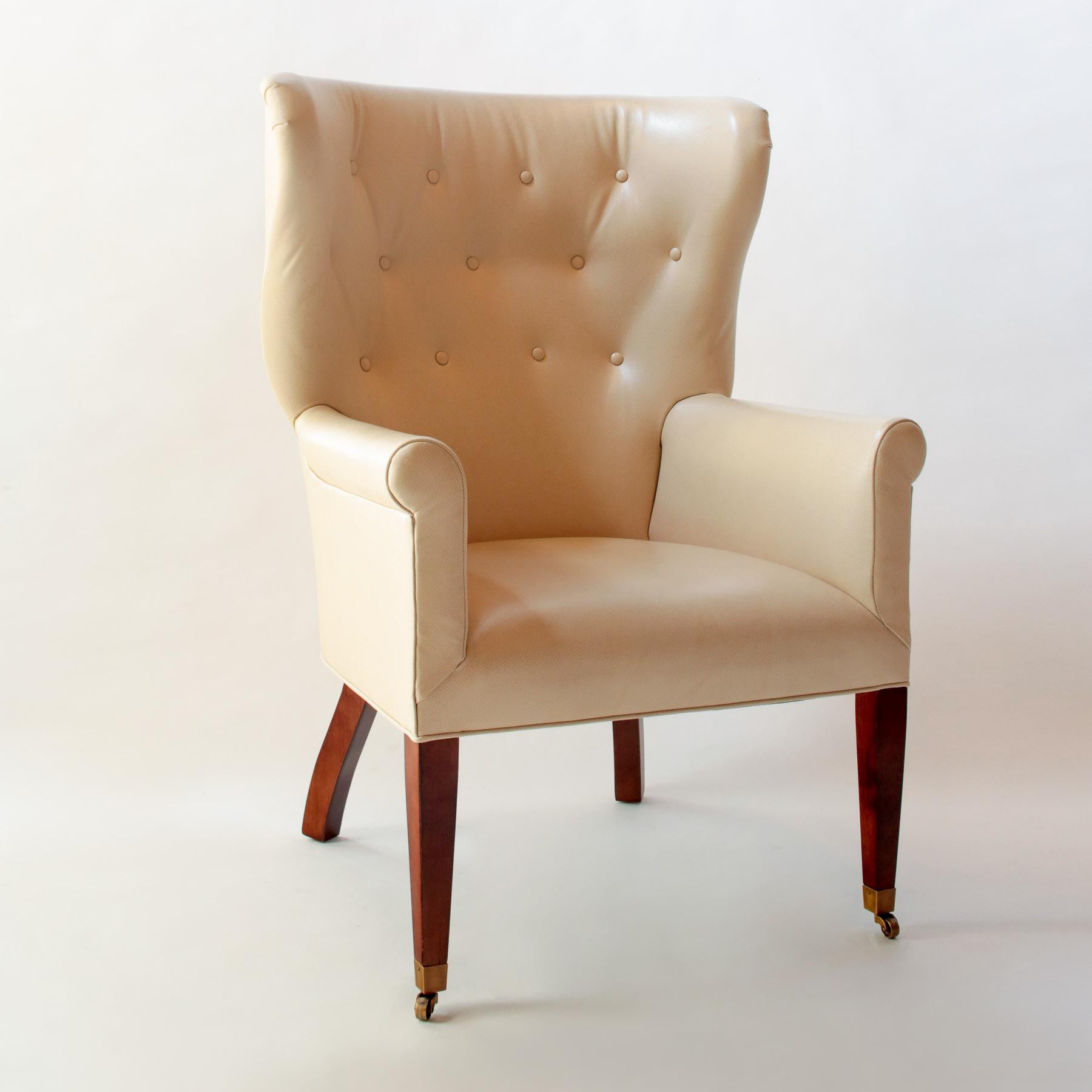 Contemporary/Transitional Georgian style tufted barrel back wing chair with legs in a mahogany finish, the front two legs terminating in brass casters. Upholstered in custom-colored Wagon Lit Edelman embossed leather.