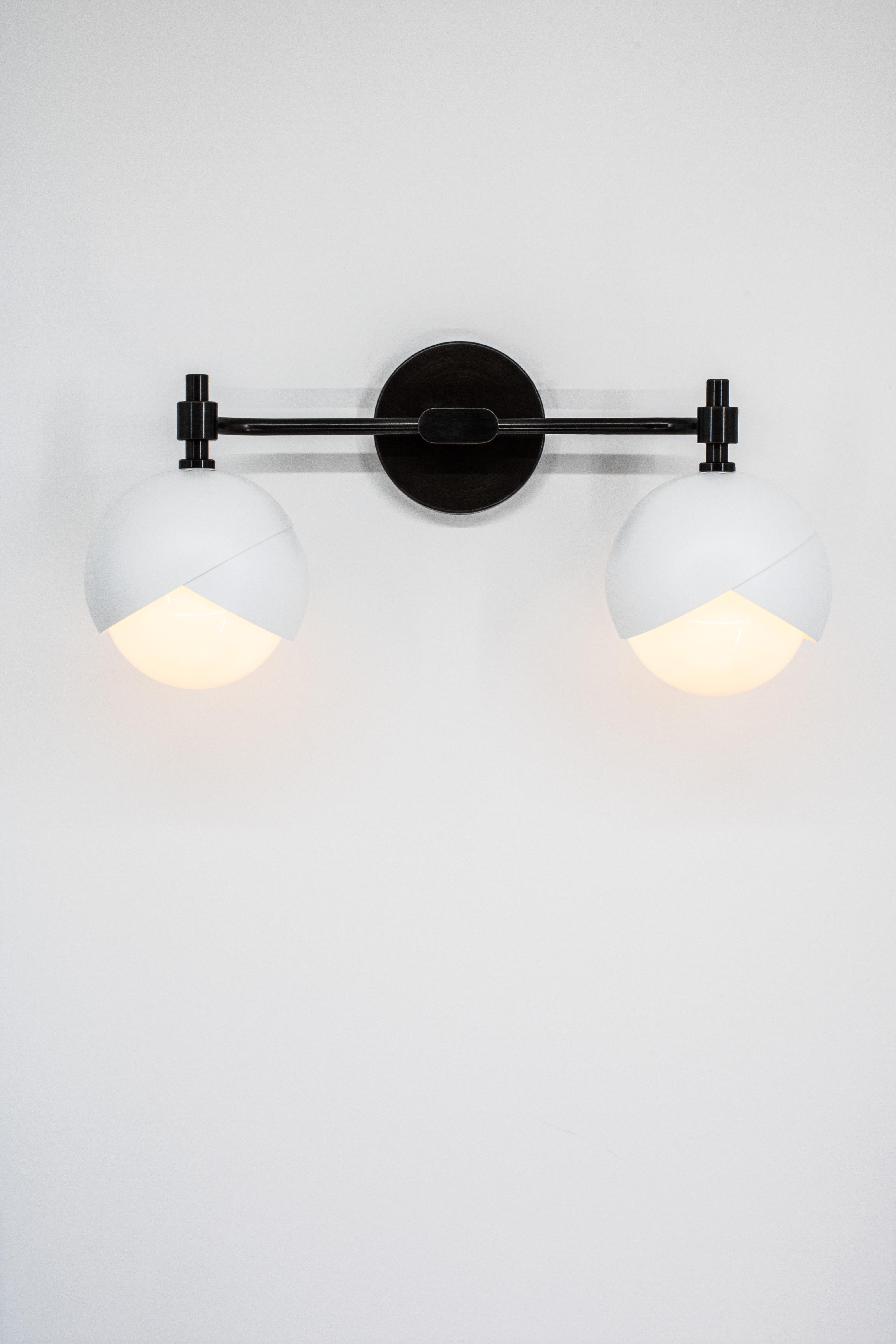 L'applique pour meuble-lavabo Benedict™ suspend deux ensembles de lumières Benedict™ à une armature horizontale en laiton. Cette applique murale est conçue pour être utilisée au-dessus d'un miroir, pour éclairer une œuvre d'art ou comme un détail
