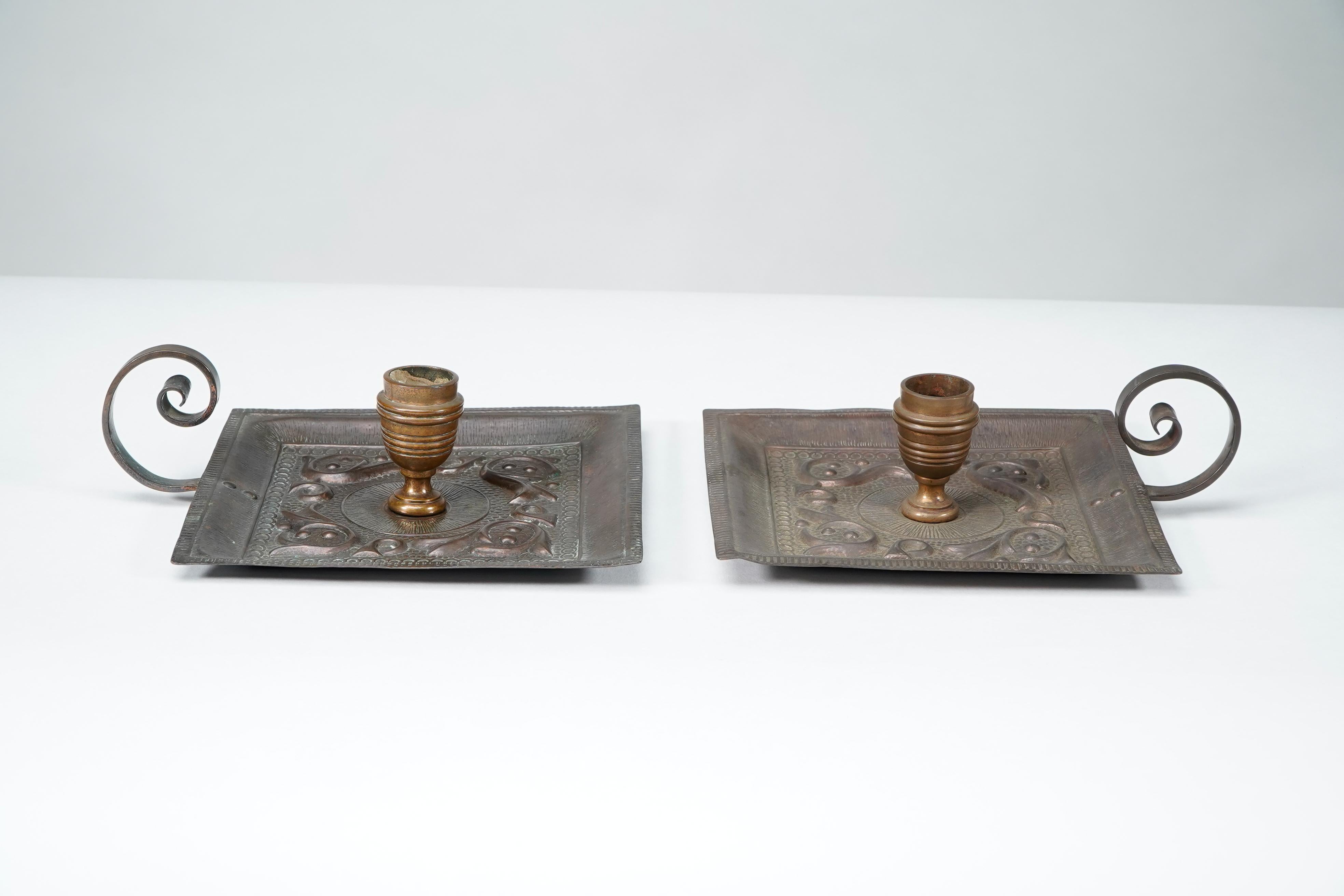 Benham & Froud Londra. Coppia di portacandele da notte in rame Decorative Crafts, con decorazioni floreali formate a mano sulle basi quadrate e manici estesi a voluta. Entrambi recano il marchio dei produttori Benham & Froud sul lato inferiore delle