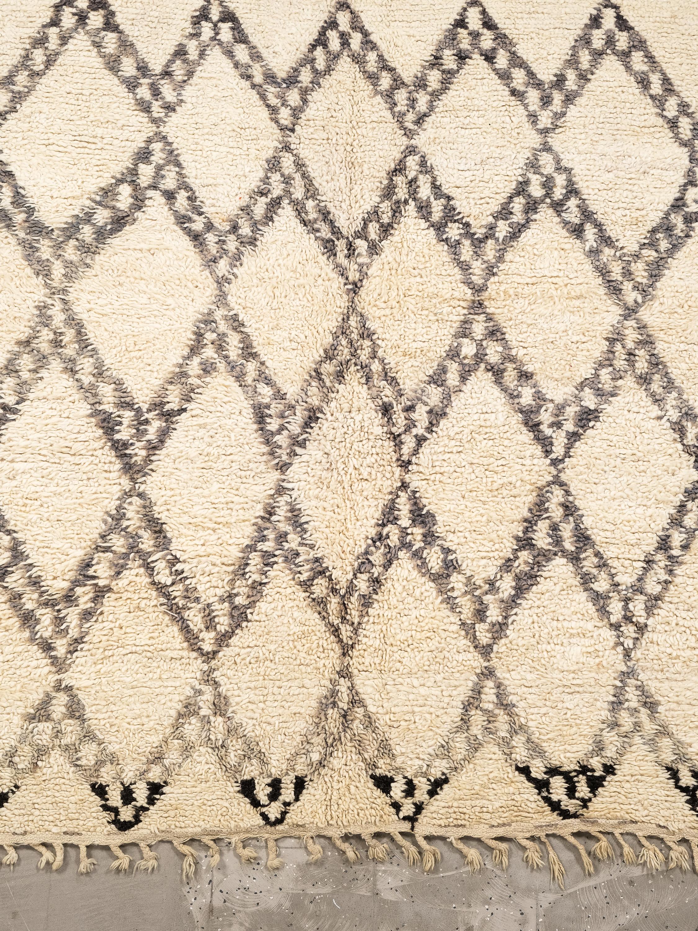 Un magnifique tapis Beni Ouarain, tissé à la main par des artisans berbères dans les montagnes du Moyen Atlas au Maroc. Cette pièce présente une base douce blanc crème, élégamment ornée d'un motif classique de treillis de diamants dans des tons