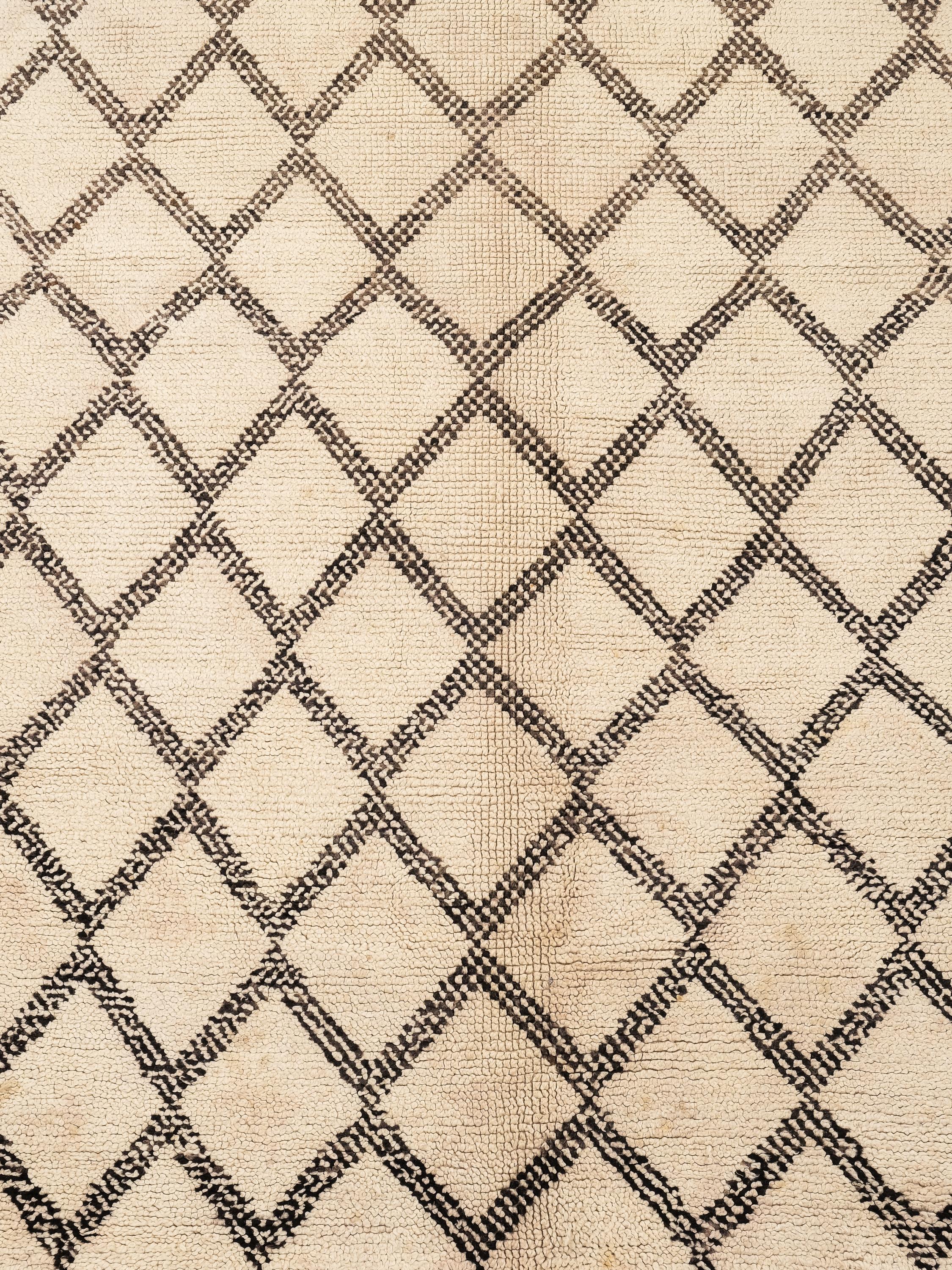 Un magnifique tapis Beni Ouarain, tissé à la main par des artisans berbères dans les montagnes du Moyen Atlas au Maroc. Cette pièce présente une base douce blanc crème, élégamment ornée d'un motif classique de treillis de diamants dans des tons