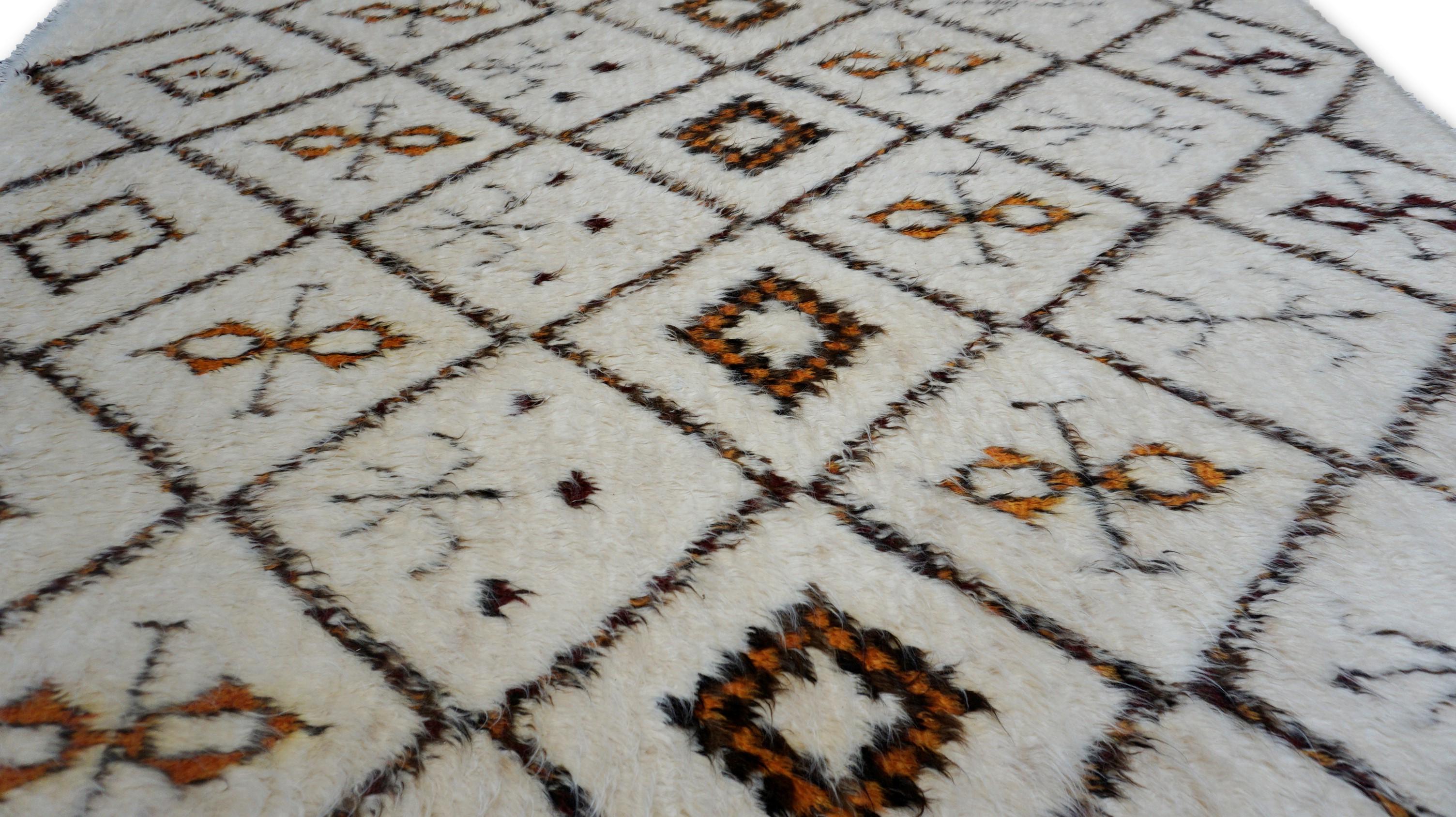 Dieser Teppich ist ein handgeknüpfter Wollteppich im Stil von Beni Ourain, inspiriert von den ikonischen Berbermustern. Dieses Stück zeichnet sich durch eine hochflorige Konstruktion und ein klassisches Rautengittermuster aus, das mit Stammesmotiven