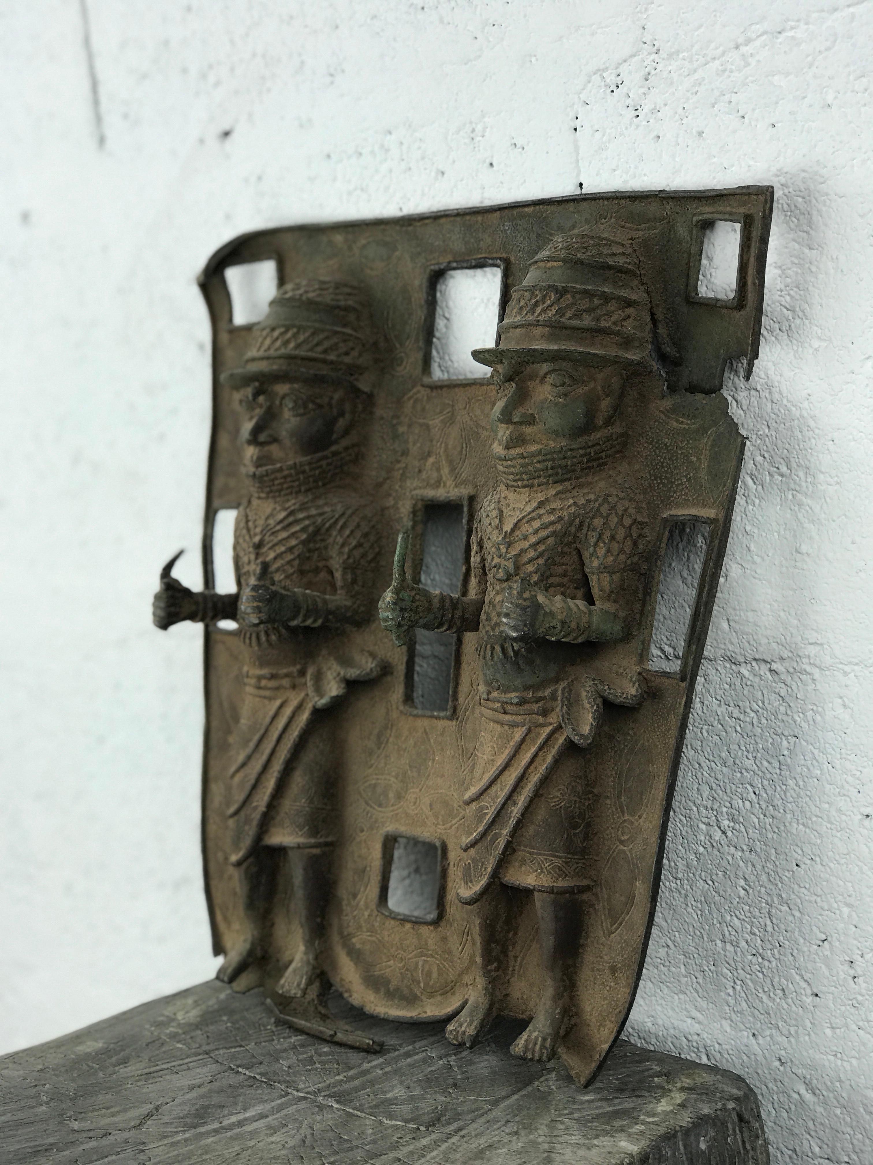 Placca a rilievo in bronzo proveniente dal Regno di Benin, in Nigeria, fusa con la tradizionale tecnica a cera persa tipica dei laboratori reali di Edo.
Raffigura due guerrieri in armatura cerimoniale, in piedi uno accanto all'altro, che indossano