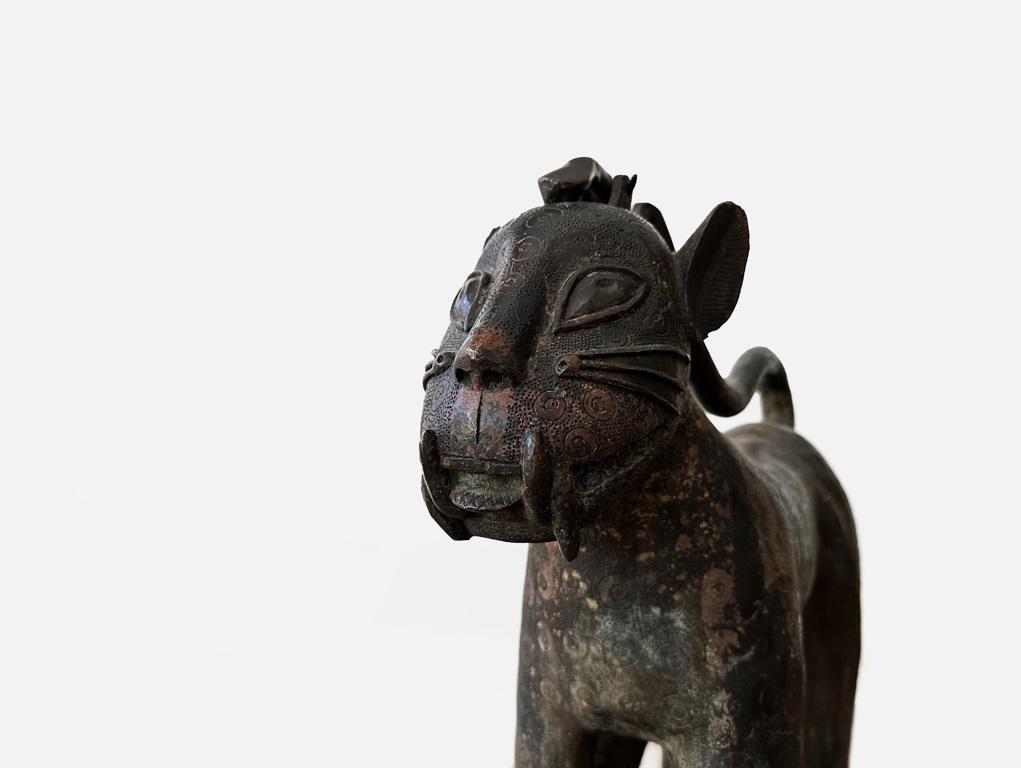 Nach den originalen Benin-Bronzen stellt diese Statue einen großen stehenden Leoparden mit umgedrehtem Schwanz und ungewöhnlich langen Beinen aus der Mitte des 20. Jahrhunderts dar, der im gleichen Gussverfahren hergestellt wurde, aber alle Merkmale