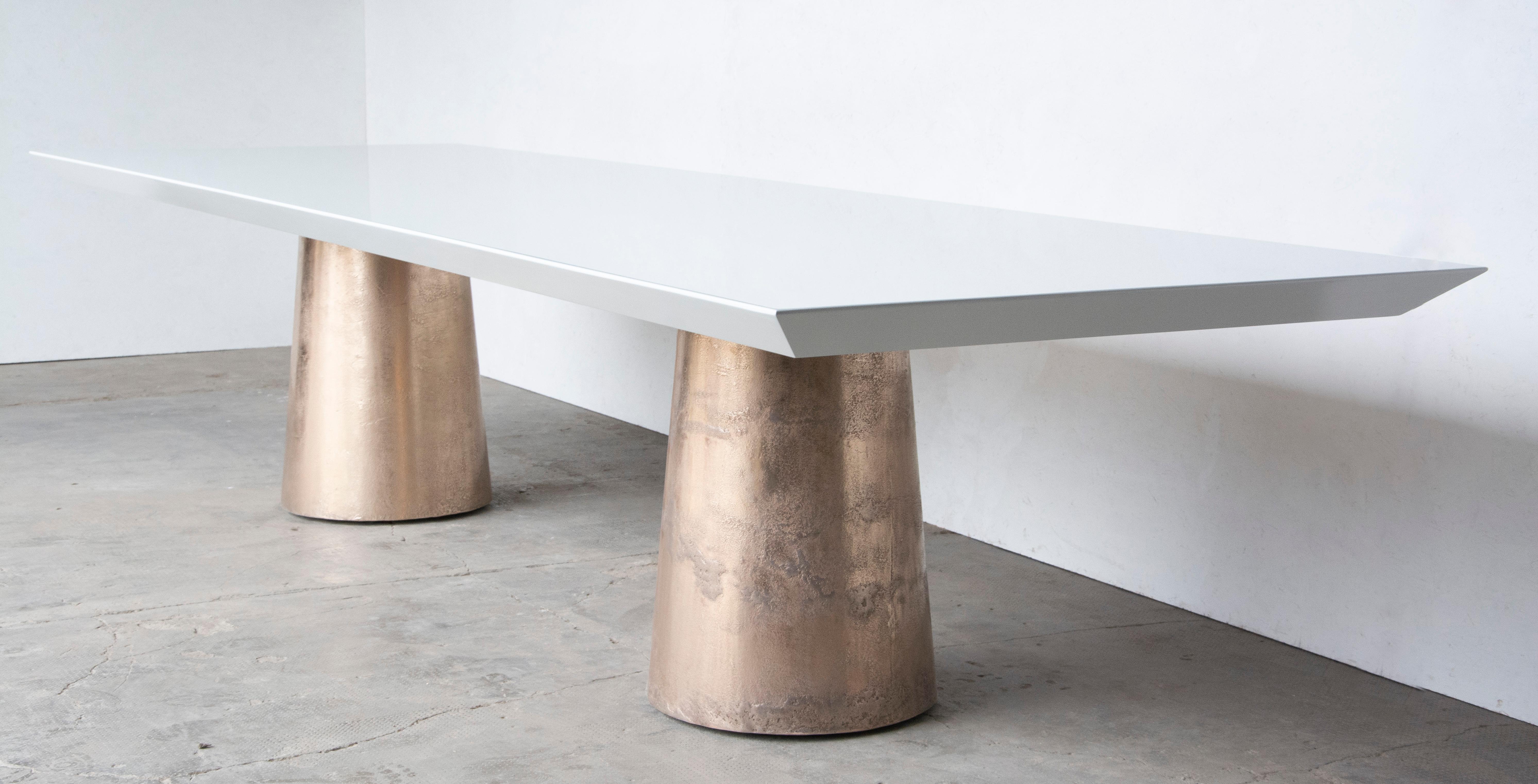 The Benino Table features two cast bronze bases that are only partially polished in order to highlight the imperfections that evidence the burnt earth that once surrounded them during the casting process. Its top, by contrast, is finished smooth and